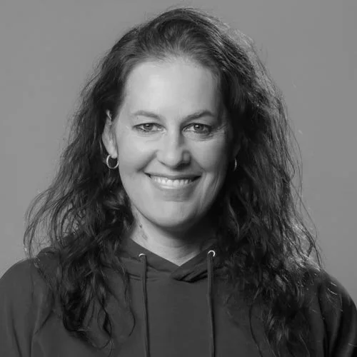 Black and white photo of a woman with curly hair smiling, wearing hoop earrings and a hoodie.