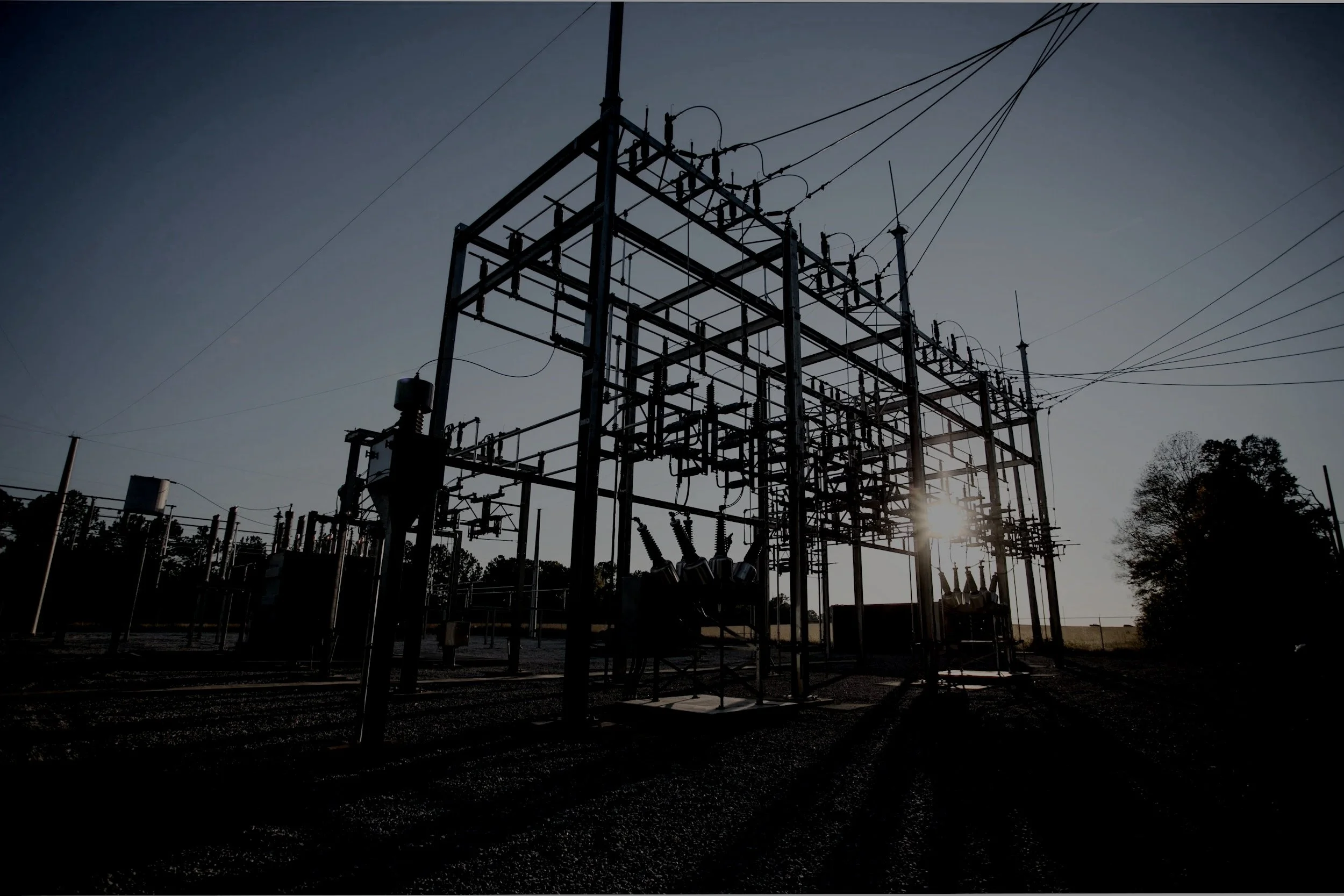 Silhouette of an electrical substation at sunset with visible power lines against the sky.