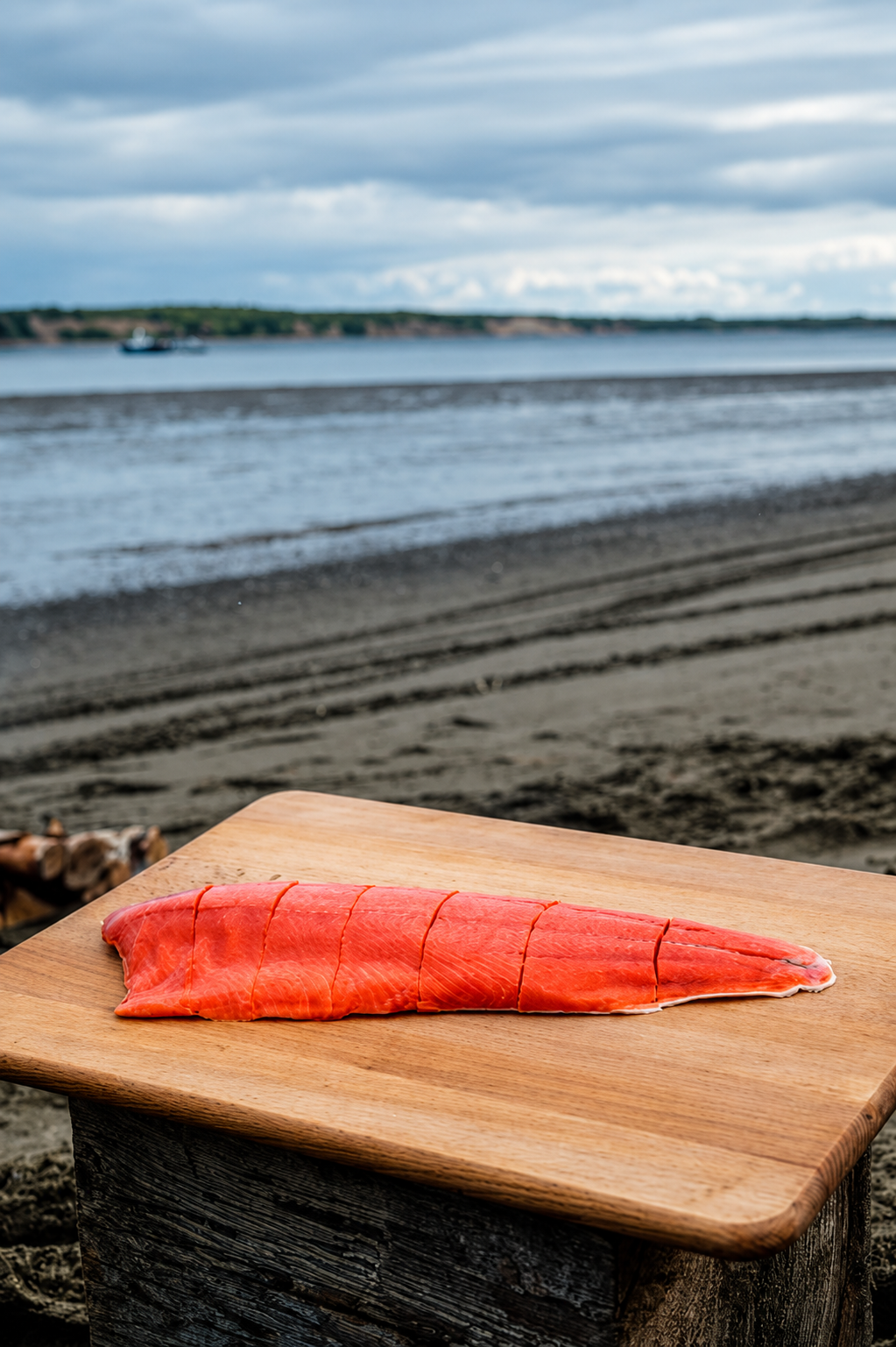 Sliced raw salmon fillet on a wooden cutting board at a beach.