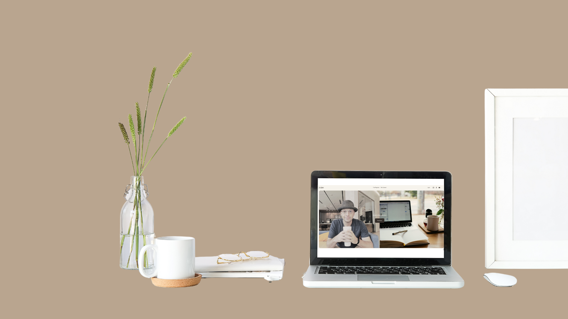 A minimalist workspace with a beige background featuring a glass vase with green plant stalks, a white mug on a brown coaster, a white notebook with glasses on top, a laptop displaying a video call with a person wearing a hat, and a white computer monitor with a white mouse.