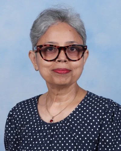Portrait of an older woman with glasses, short gray hair, smiling, wearing a white collared shirt, against a blue background.