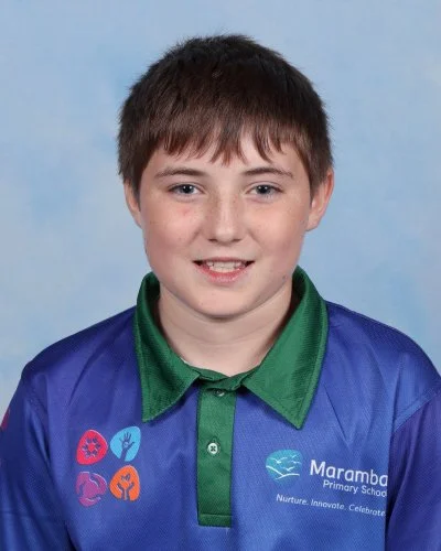 Young boy with short brown hair, wearing a blue sports jersey, smiling, against a light blue background.
