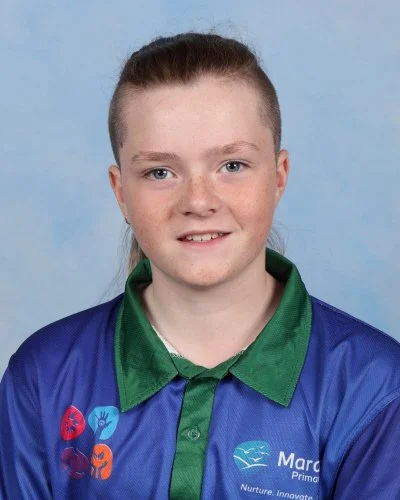 A young woman with long light brown hair smiling, wearing a blue polo shirt, against a light blue background.