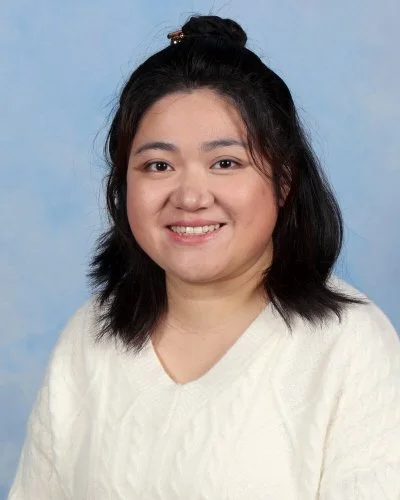 Portrait of a woman in a yellow shirt smiling against a blue background.