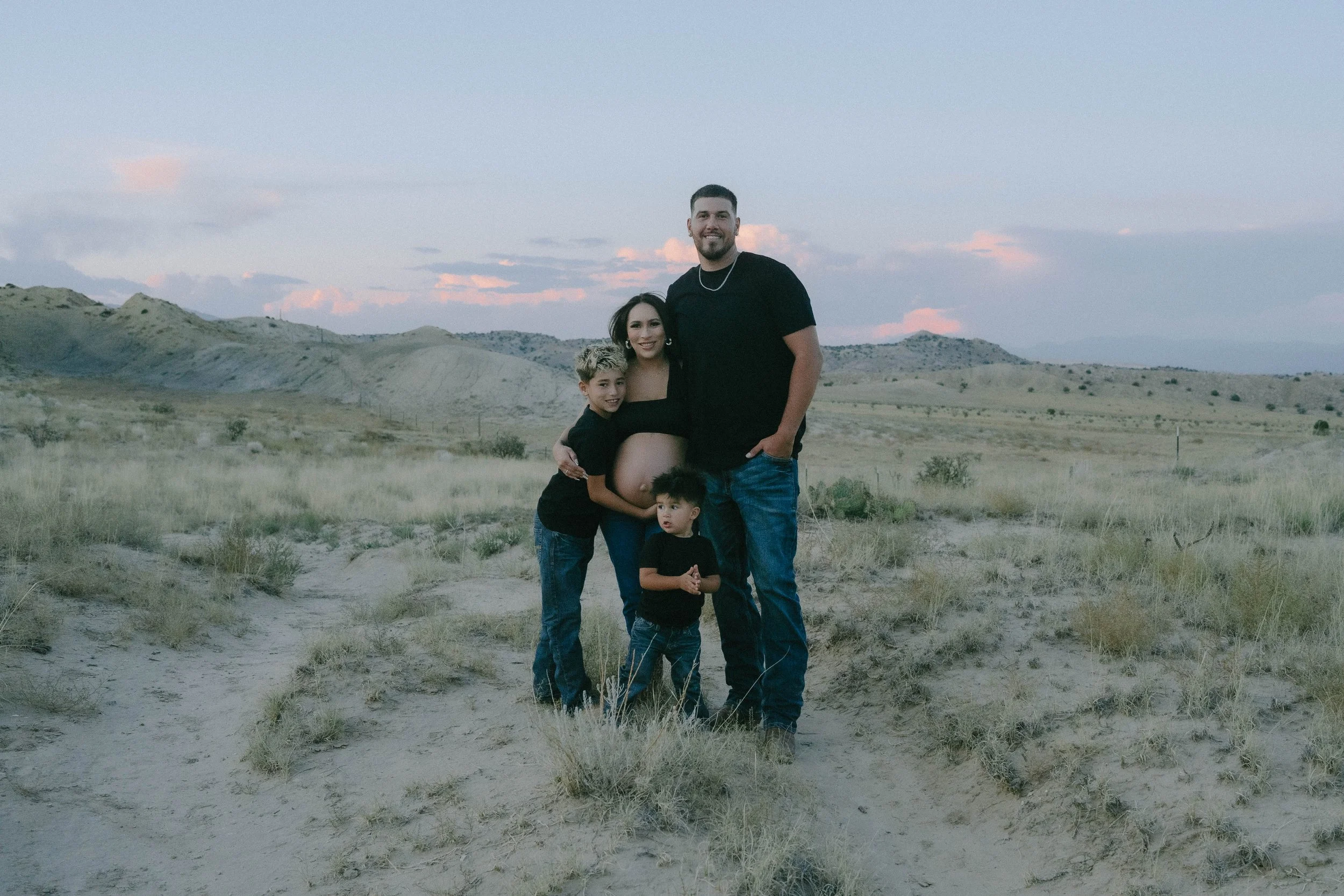 A family of four shares a quiet, loving moment with New Mexico's desert mountains in the background - photographed by Paul Porras Photography in Albuquerque, New Mexico.