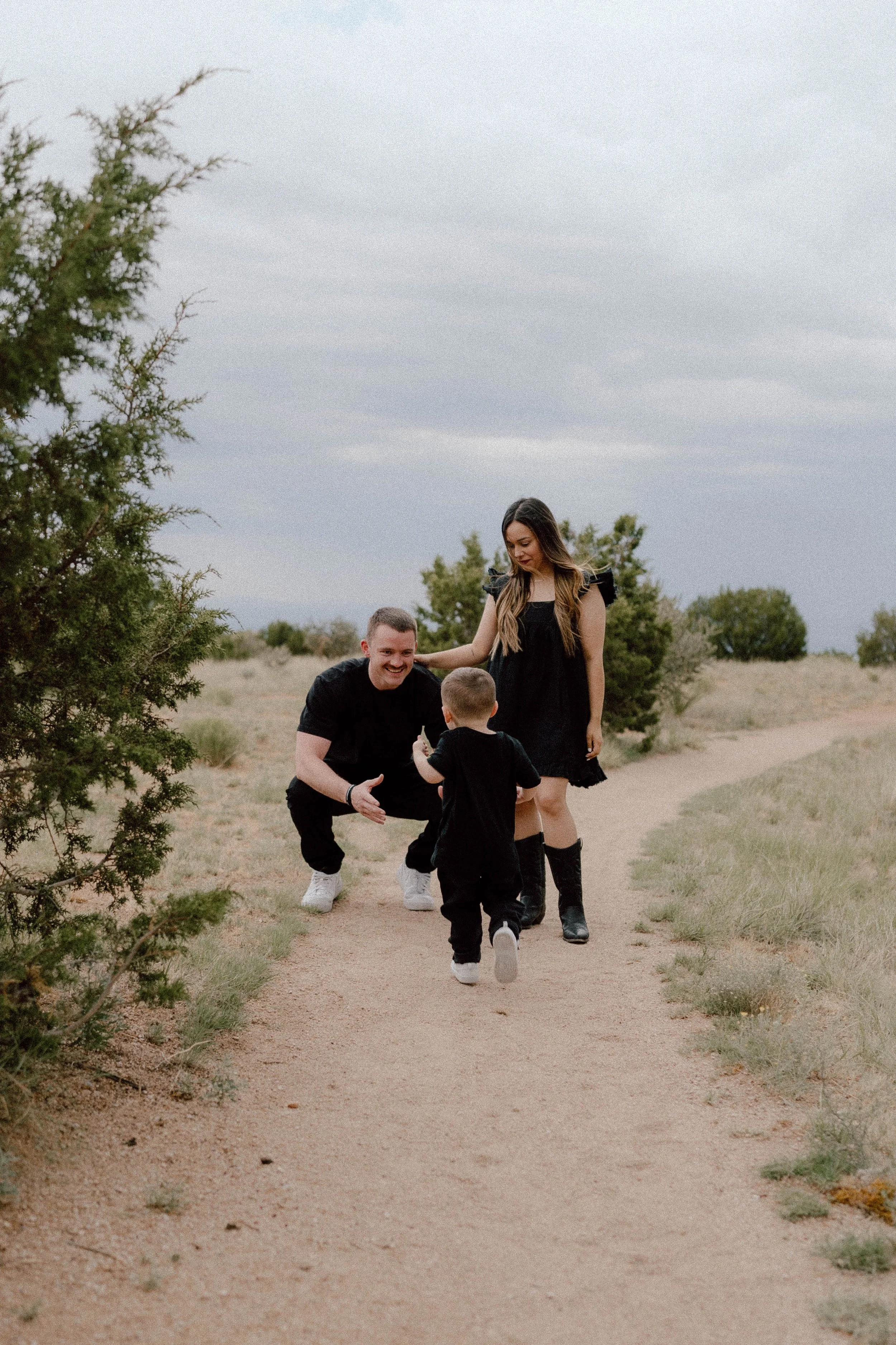 A young family walks through a golden field in New Mexico, their toddler running joyfully ahead - captured by Paul Porras Photography in Albuquerque, New Mexico.