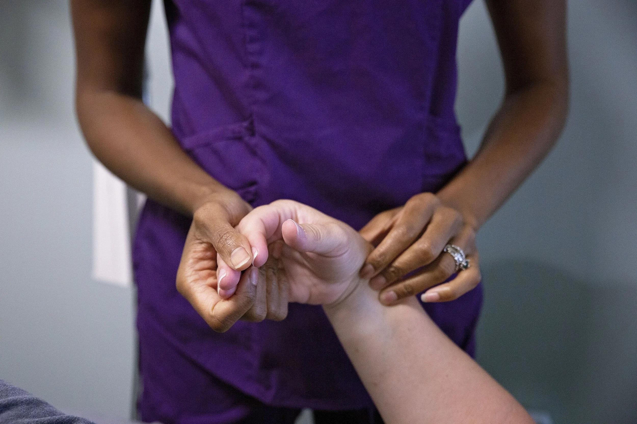 A healthcare professional taking a patient's wrist pulse in a clinical setting.