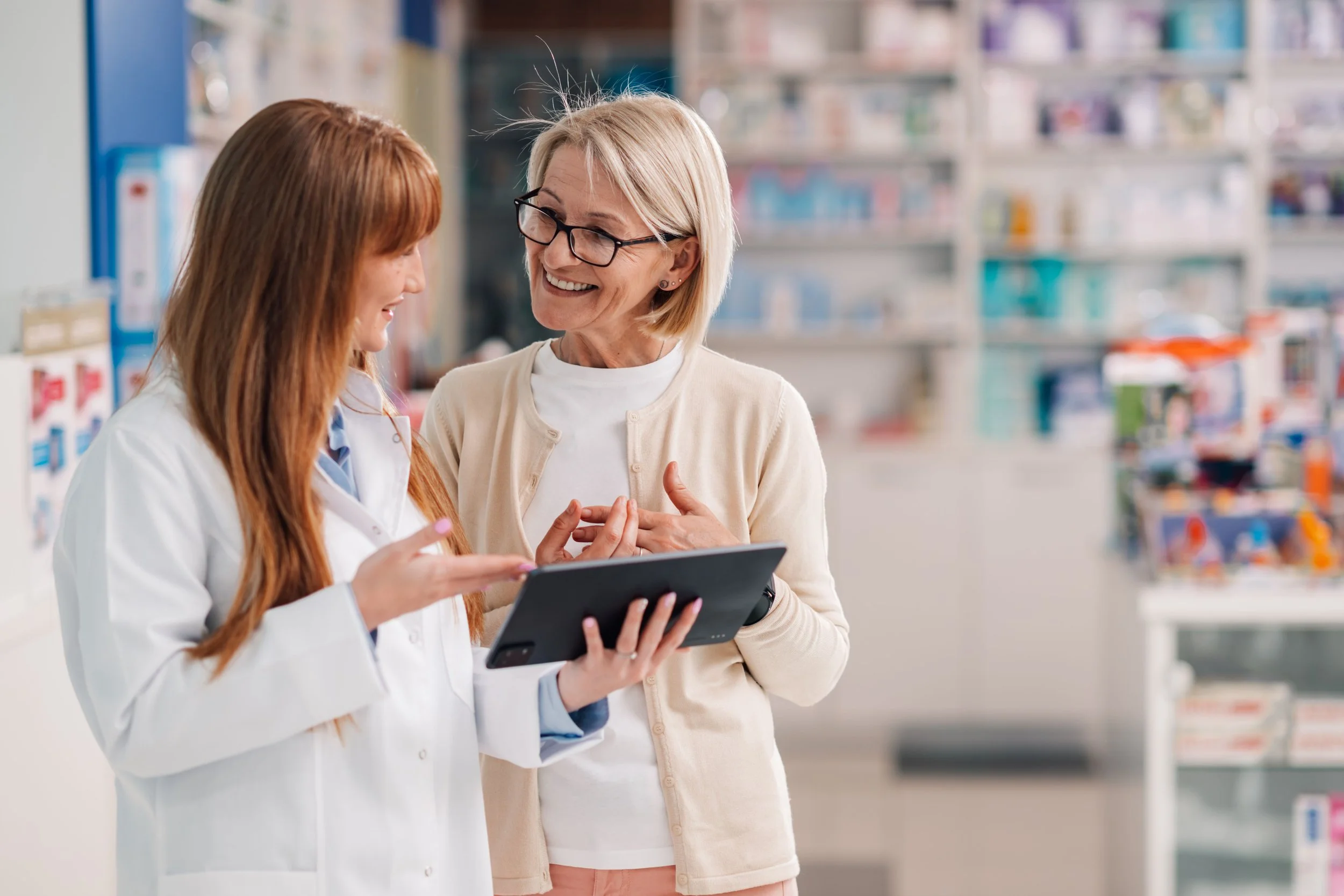 Pharmacist and customer talking in pharmacy, looking at a tablet.