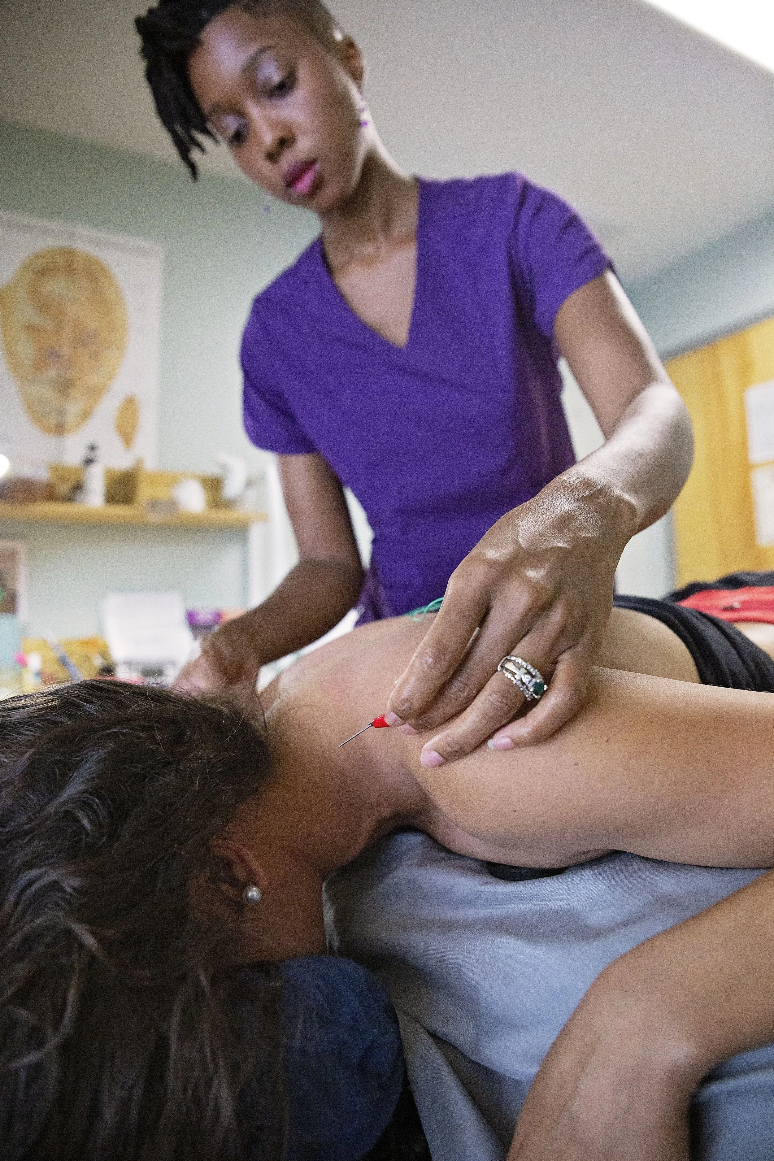 A healthcare professional administering an injection to a woman lying on a medical bed in a clinic room.