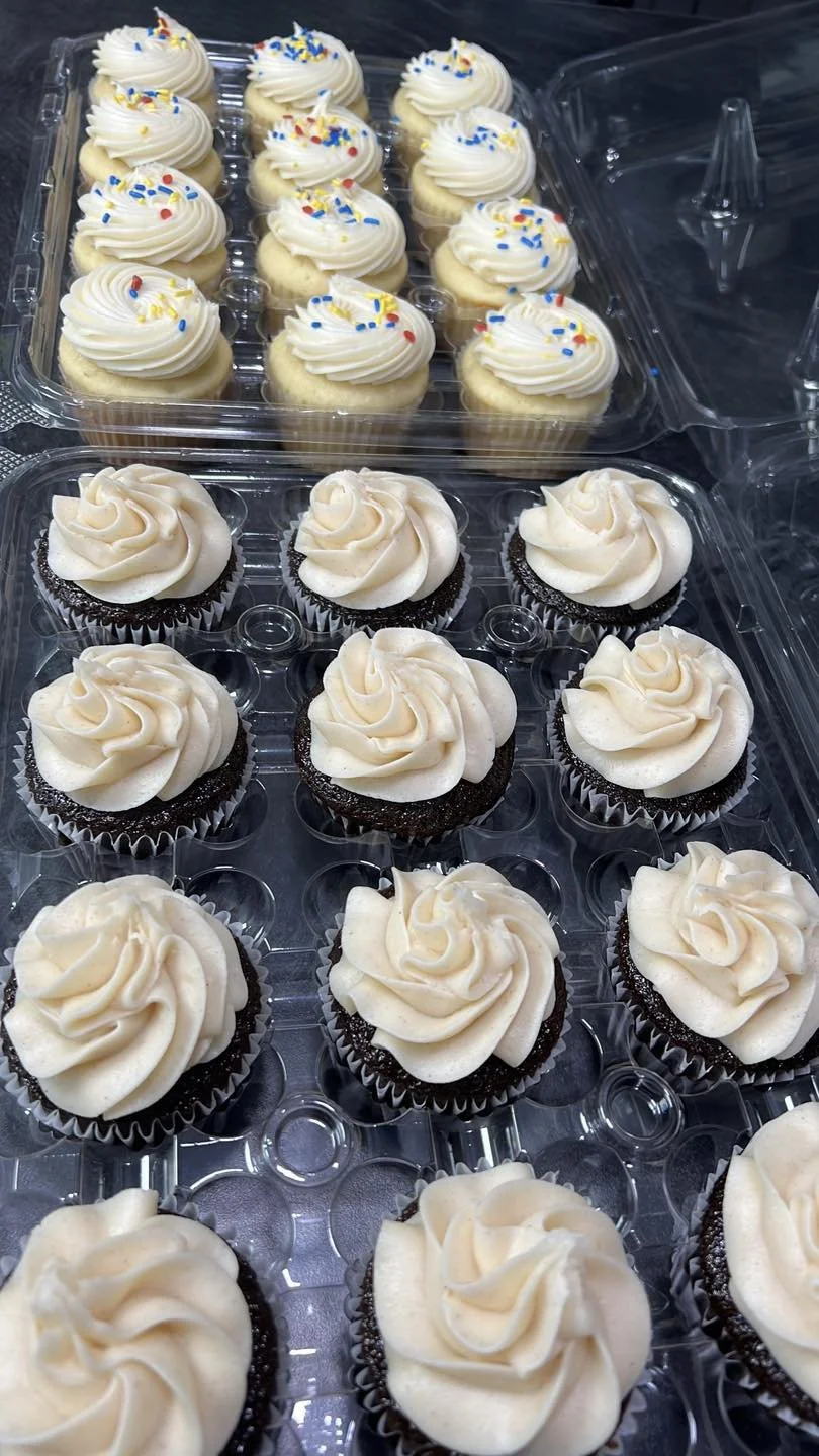 Tray of cupcakes topped with white frosting and colorful sprinkles, arranged in two rows.