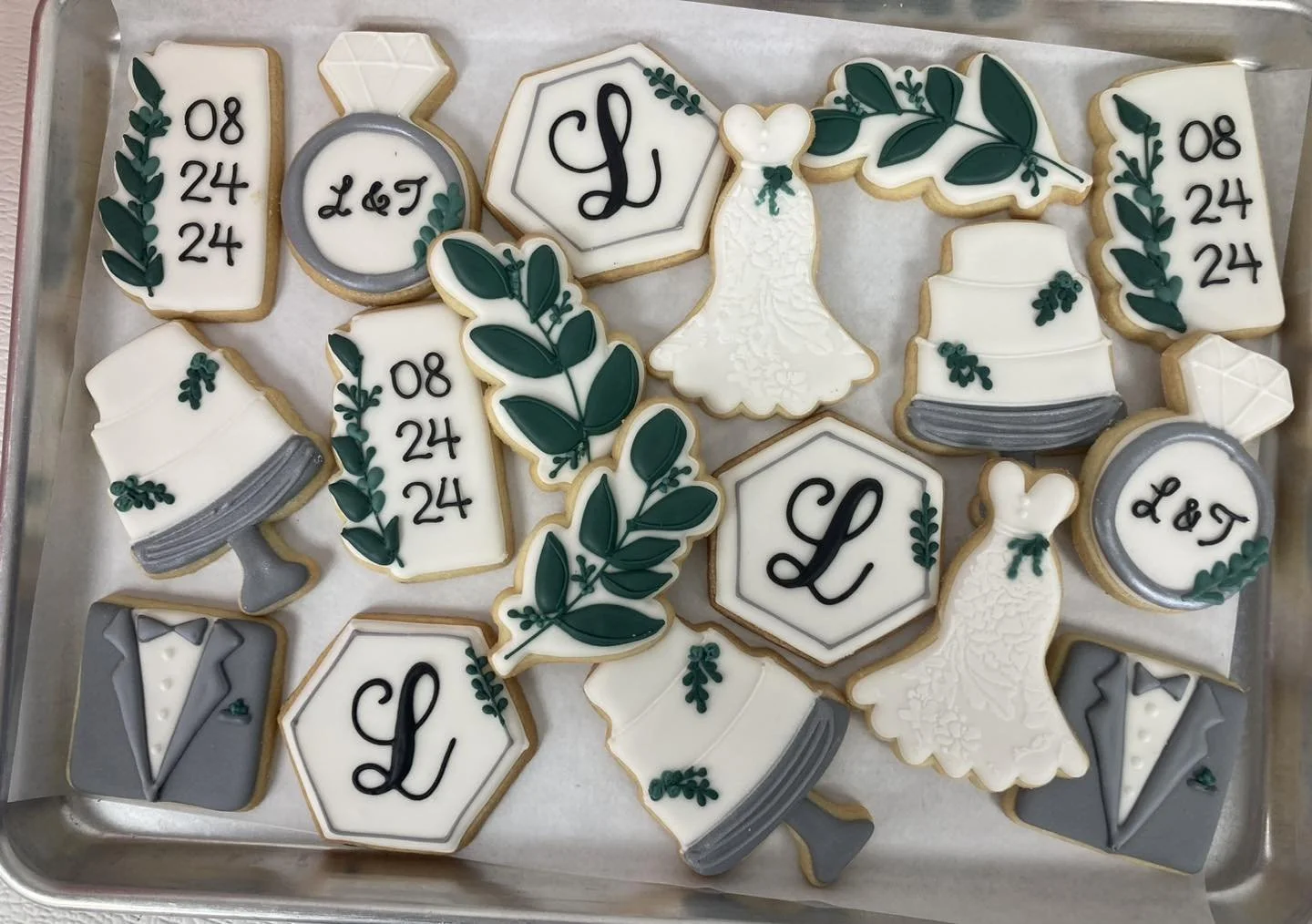 Assorted wedding cookies decorated with wedding symbols like a wedding dress, tuxedo, wedding rings,'a' letter, and date 08/24/24, with white, gray, and green colors.