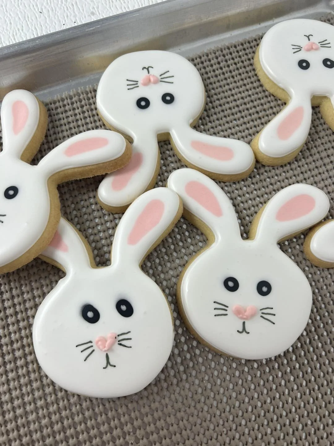 Decorated bunny cookies with white icing, pink accents, and black eyes on a textured surface.