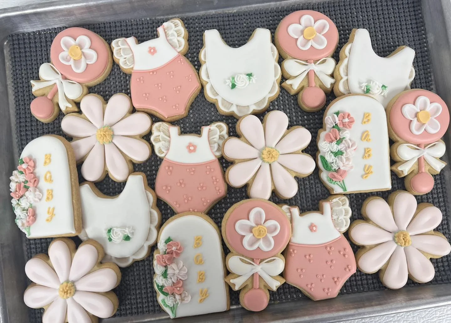Assorted decorated cookies with flowers, dresses, and the words "Baby" and "Congrats" in pastel pink, white, and yellow colors.