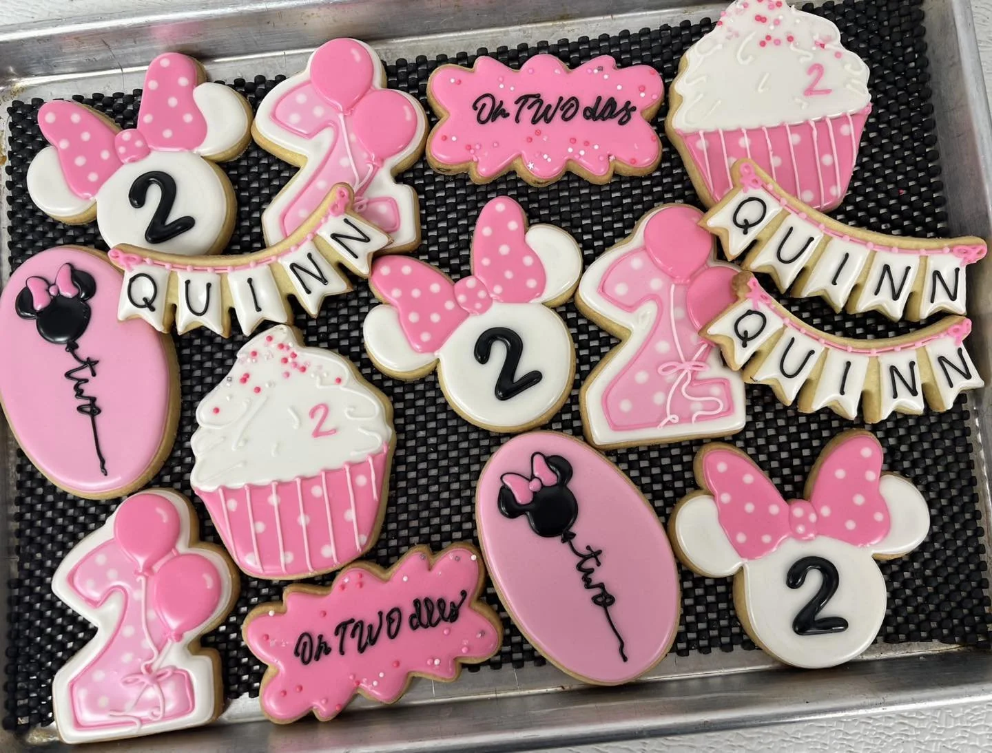 Decorated cookies with pink, white, and black icing, featuring Minnie Mouse ears, balloons, cupcakes, and birthday messages for Quinn's second birthday celebration.