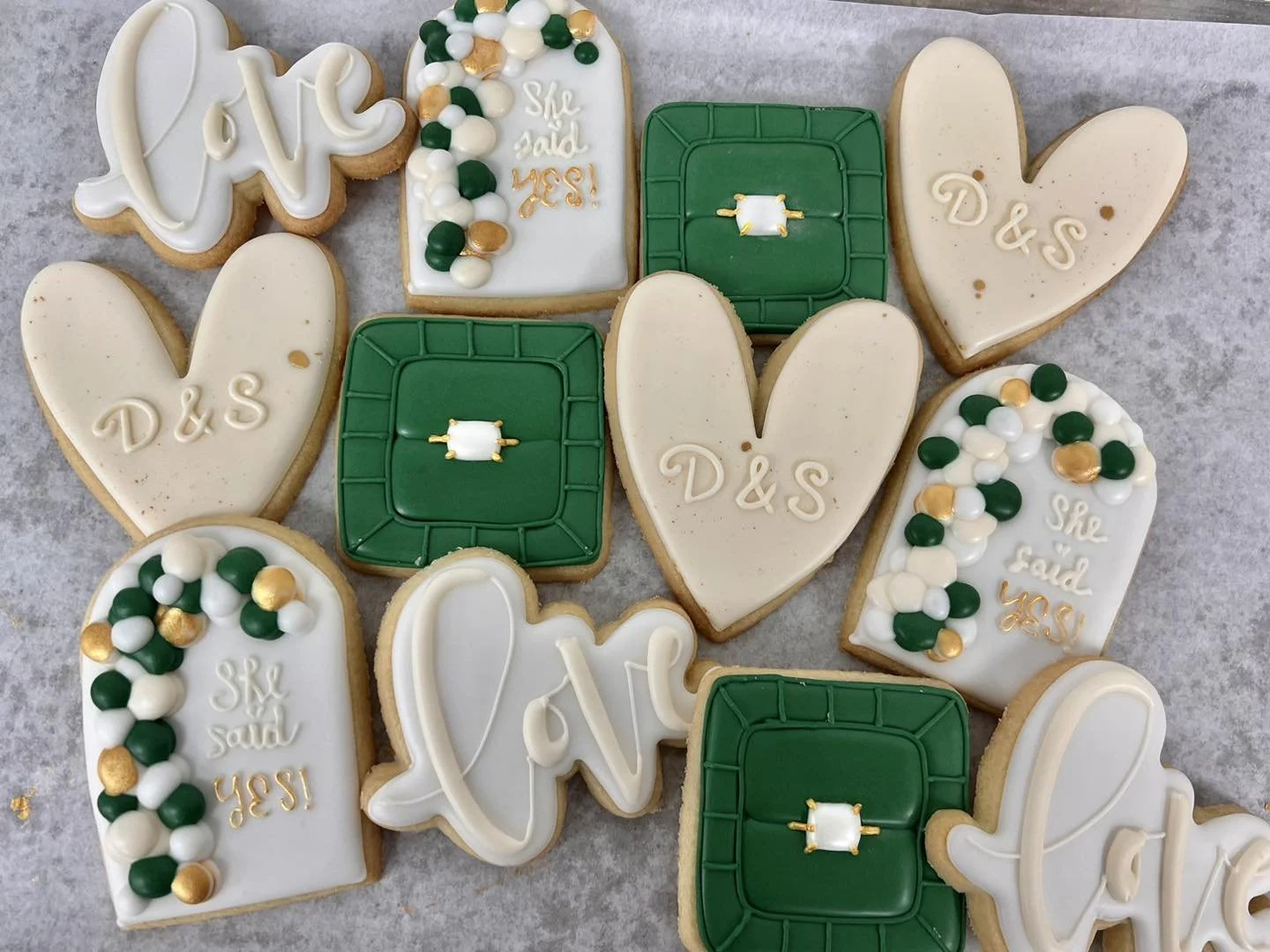 Collection of decorated cookies with green, white, and gold colors, featuring hearts, the word 'love', and a green golf bag and golf clubs pattern, likely made for a golf-themed celebration.