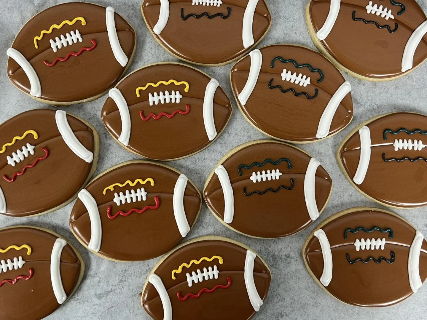 Cookies decorated to resemble American footballs, with brown icing, white icing laces, and yellow, red, blue, and black icing accents.