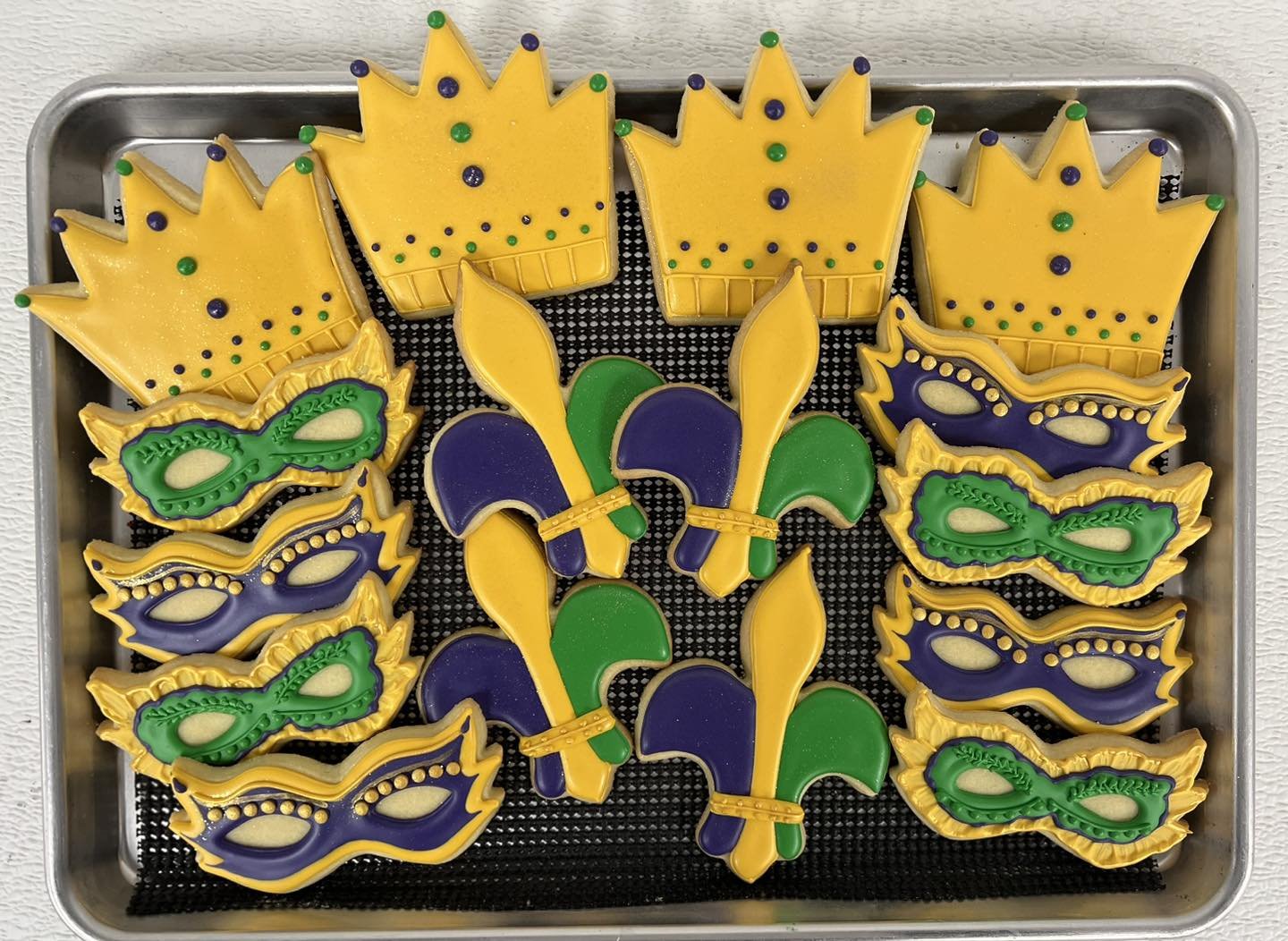 Colorfully decorated Mardi Gras cookies in the shape of crowns, masks, and flowers on a baking sheet.