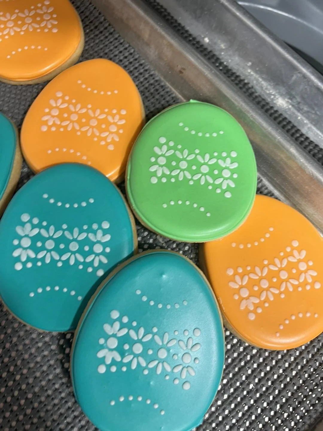 Colorful oval-shaped cookies decorated with white floral and dotted patterns in orange, green, and blue colors.