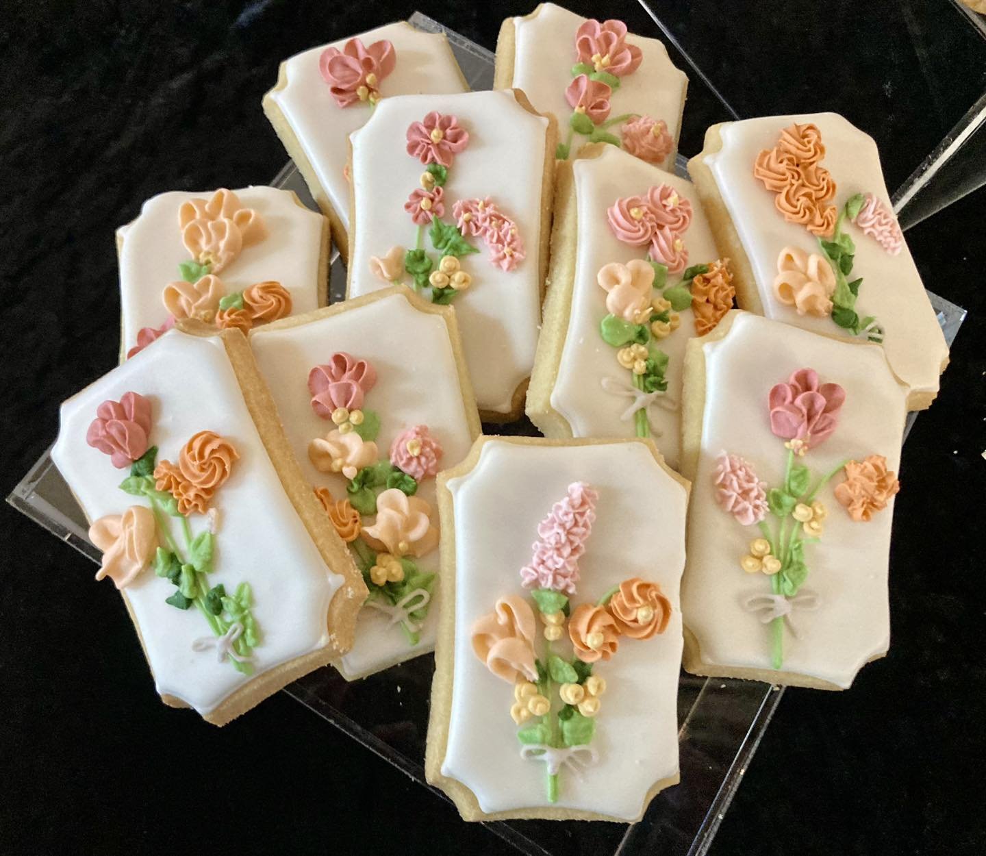 Decorated cookies with white icing and pastel-colored floral icing decorations arranged on a clear surface.