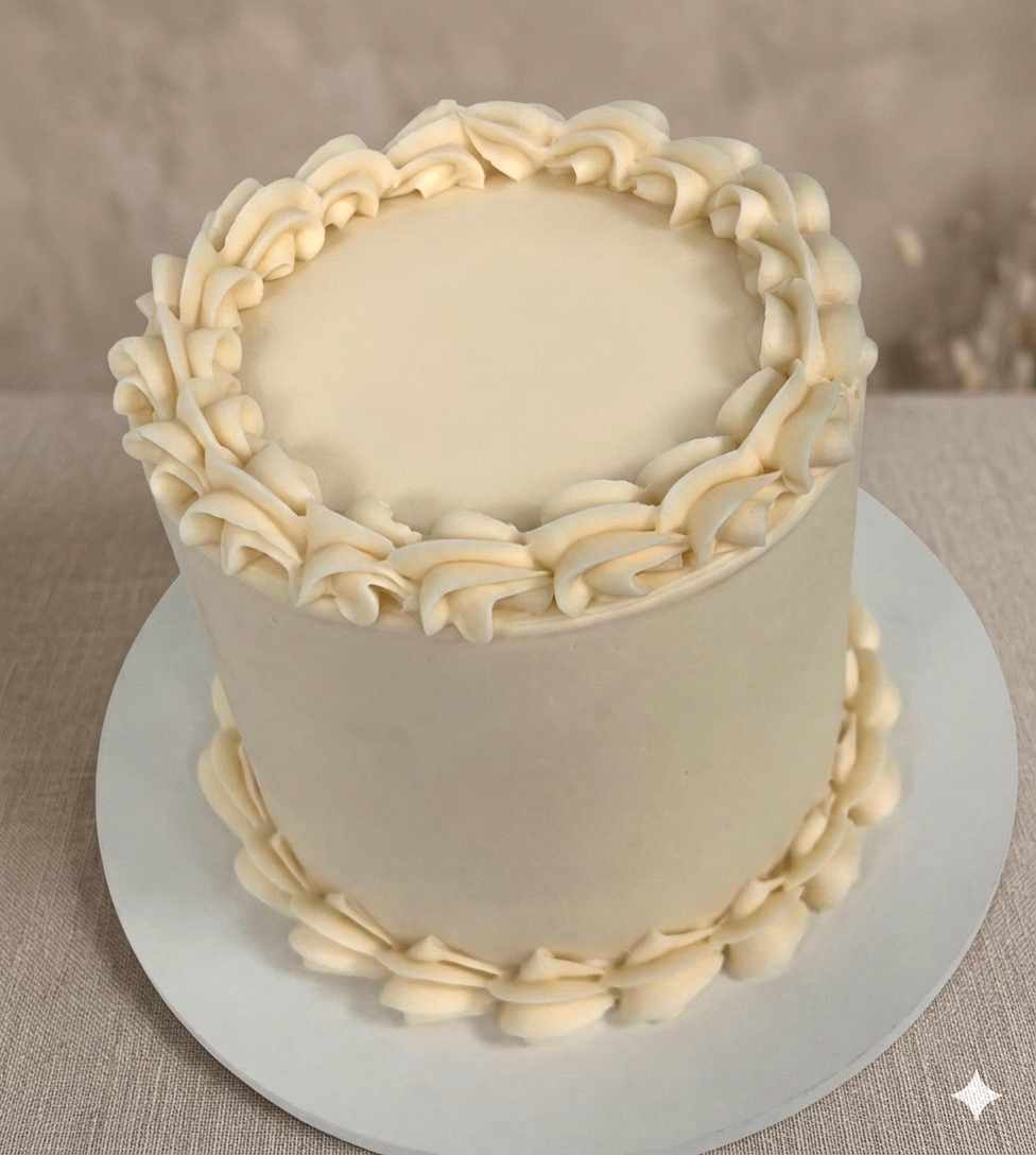 Two-tiered white wedding cake with piped white frosting border on top and bottom, placed on a white cake board.