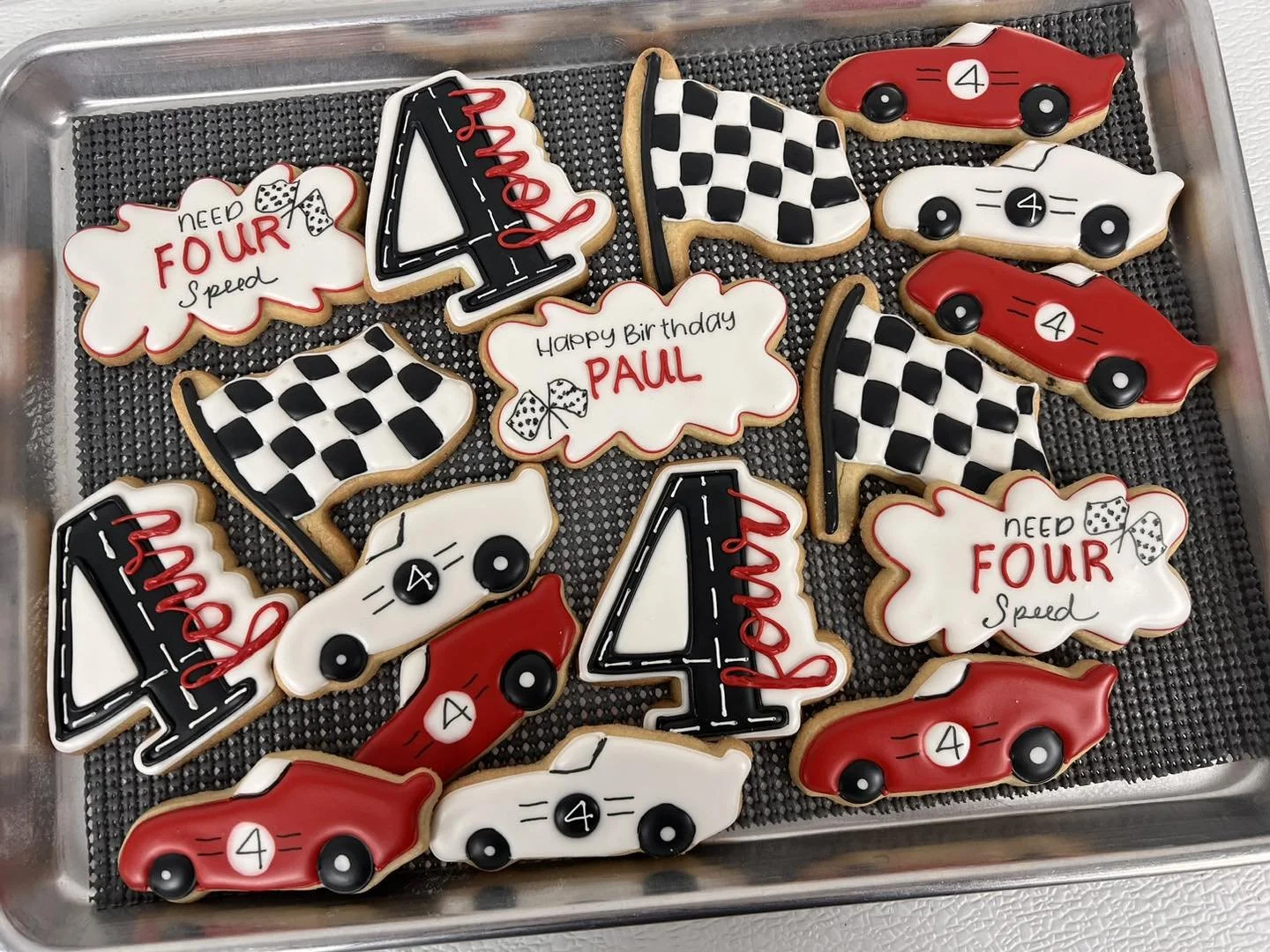 A tray of racing-themed cookies decorated with numbers, checkered flags, cars, and birthday messages in red, black, and white icing.