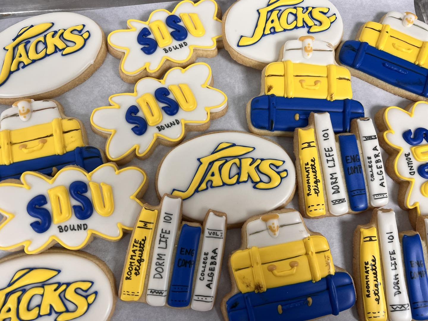 Decorated cookies with the university's logo, books, and a suitcase in school colors of yellow and blue, representing the University of Texas at Austin.