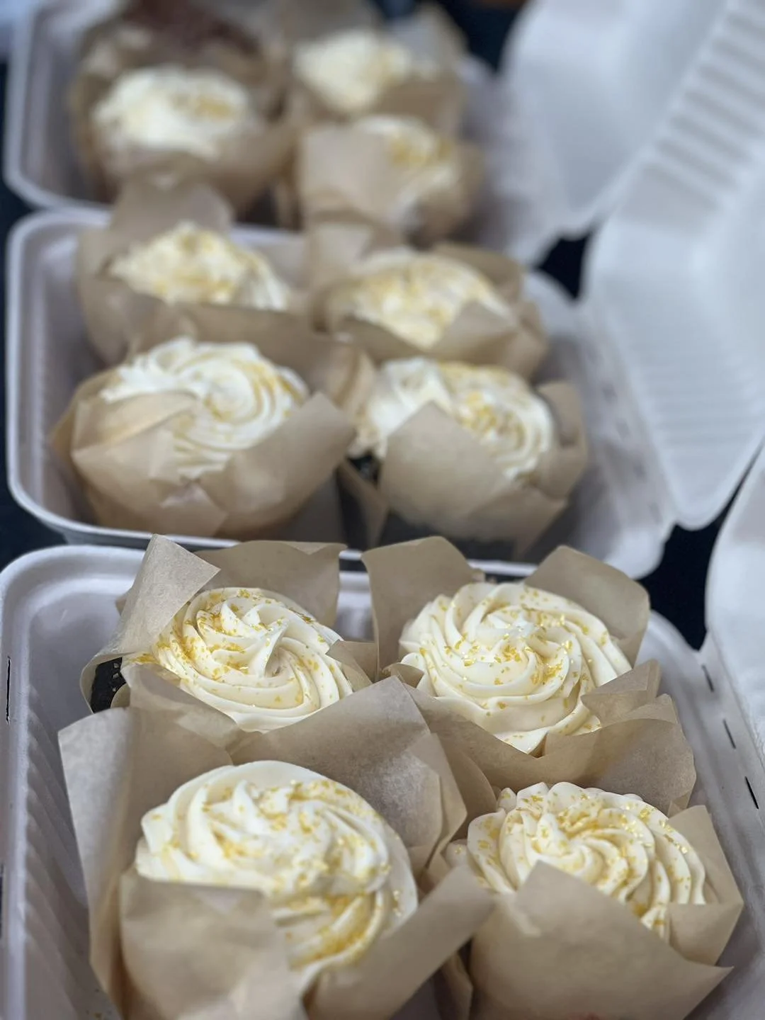Tray of cupcakes with white frosting and yellow sprinkles in paper wrappers.