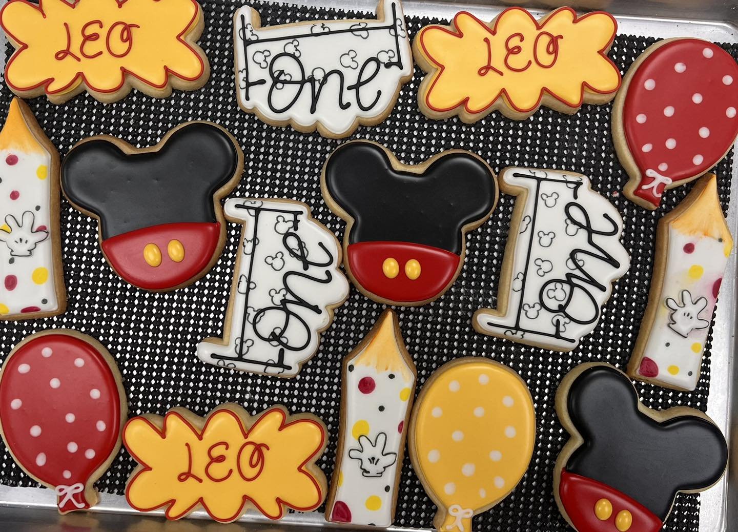 Decorative cookies on a tray with a Mickey Mouse theme, including Mickey Mouse head shapes, balloons, the word 'Leo', and other festive designs.