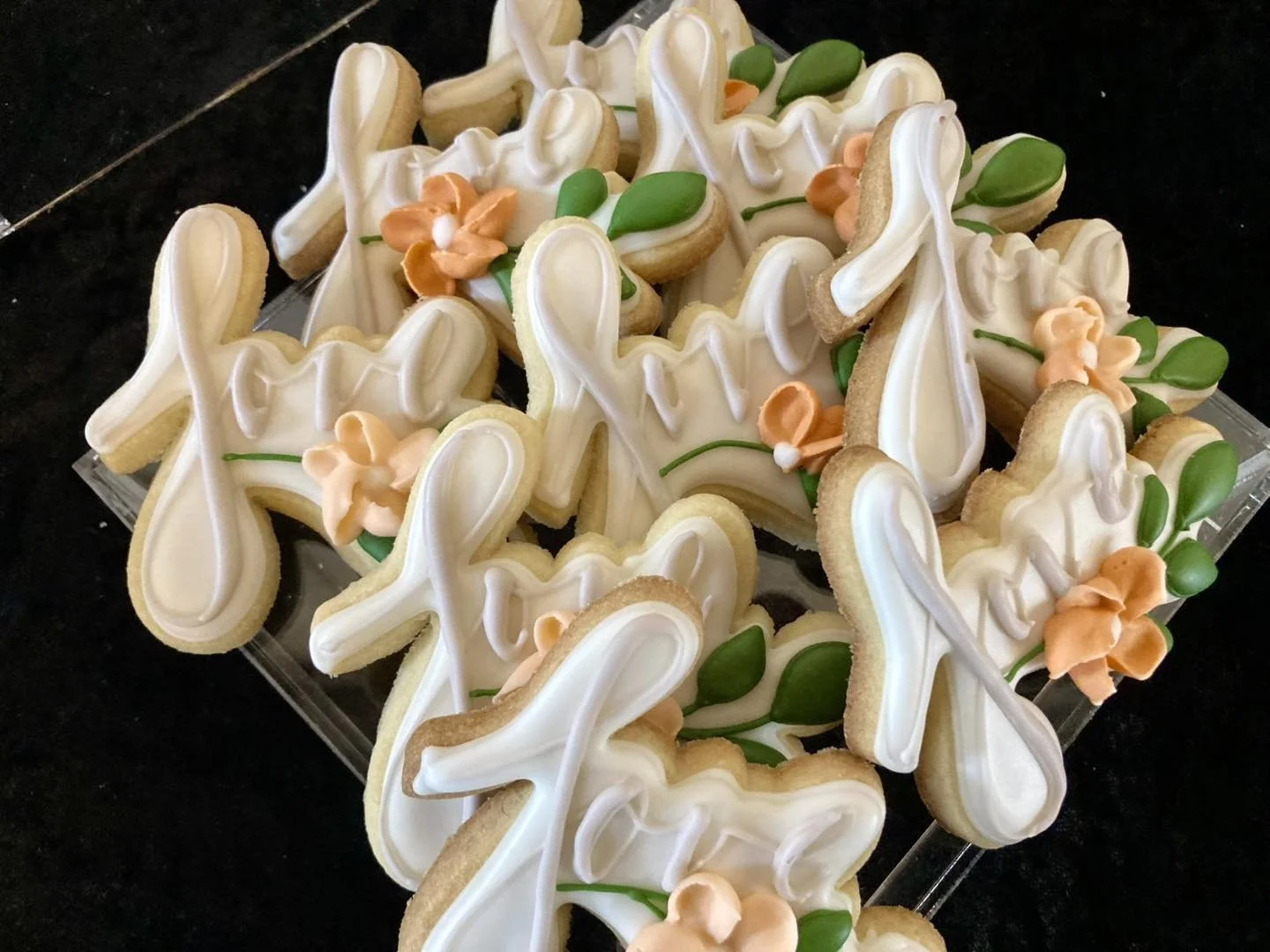 Assortment of bunny-shaped sugar cookies decorated with white icing, peach-colored flowers, and green leaves on a clear tray.