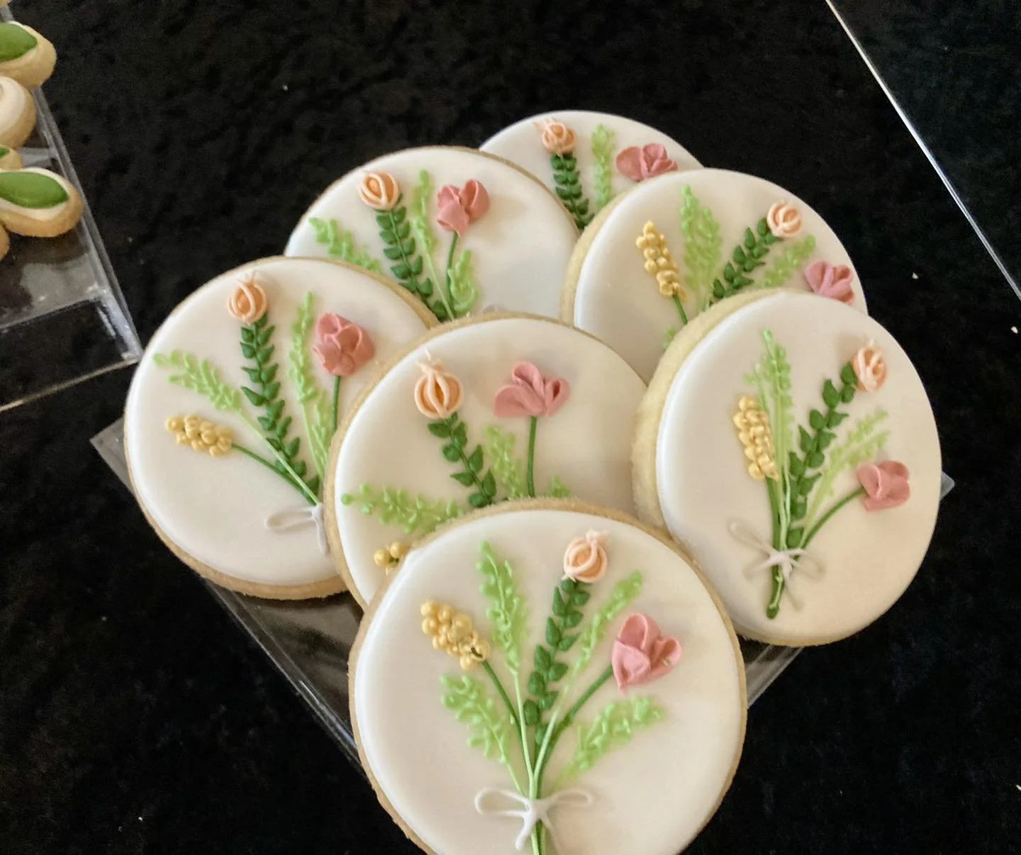 Set of decorated cookies with floral icing designs, featuring pink, yellow, and green flowers and leaves, on a black surface.