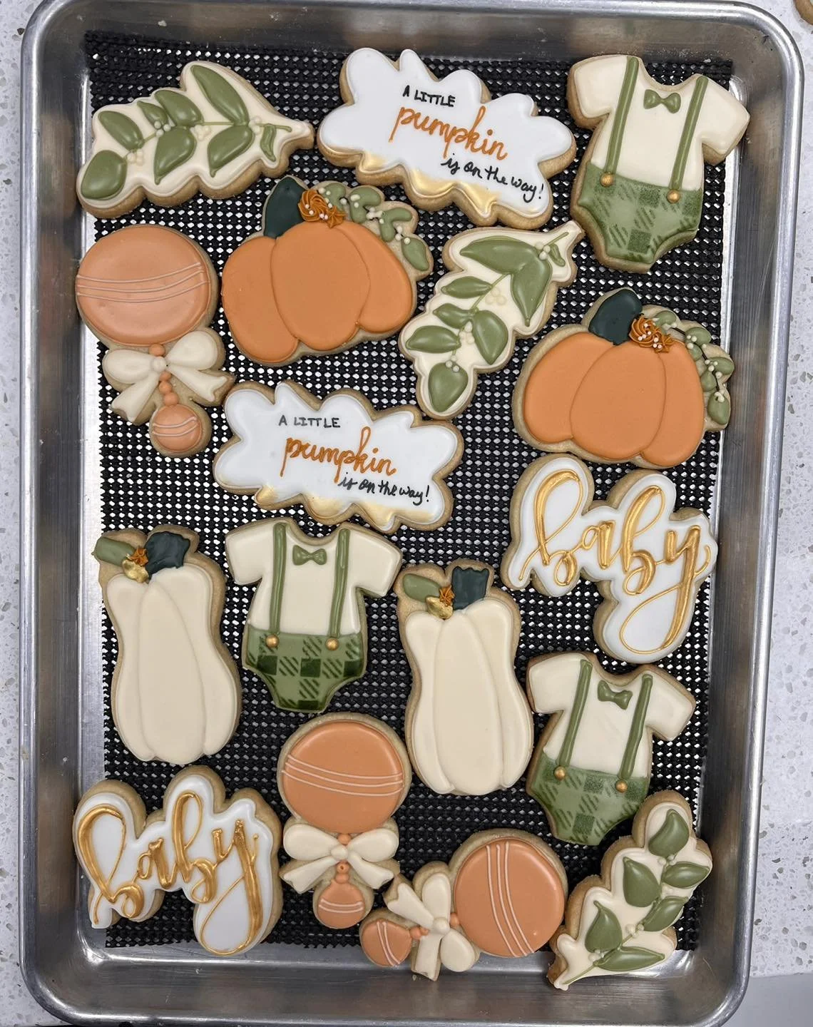 Decorated sugar cookies on a tray with autumn and baby shower themes, including pumpkins, balloons, baby onesies, and the words 'baby' and 'a little pumpkin on the way'.