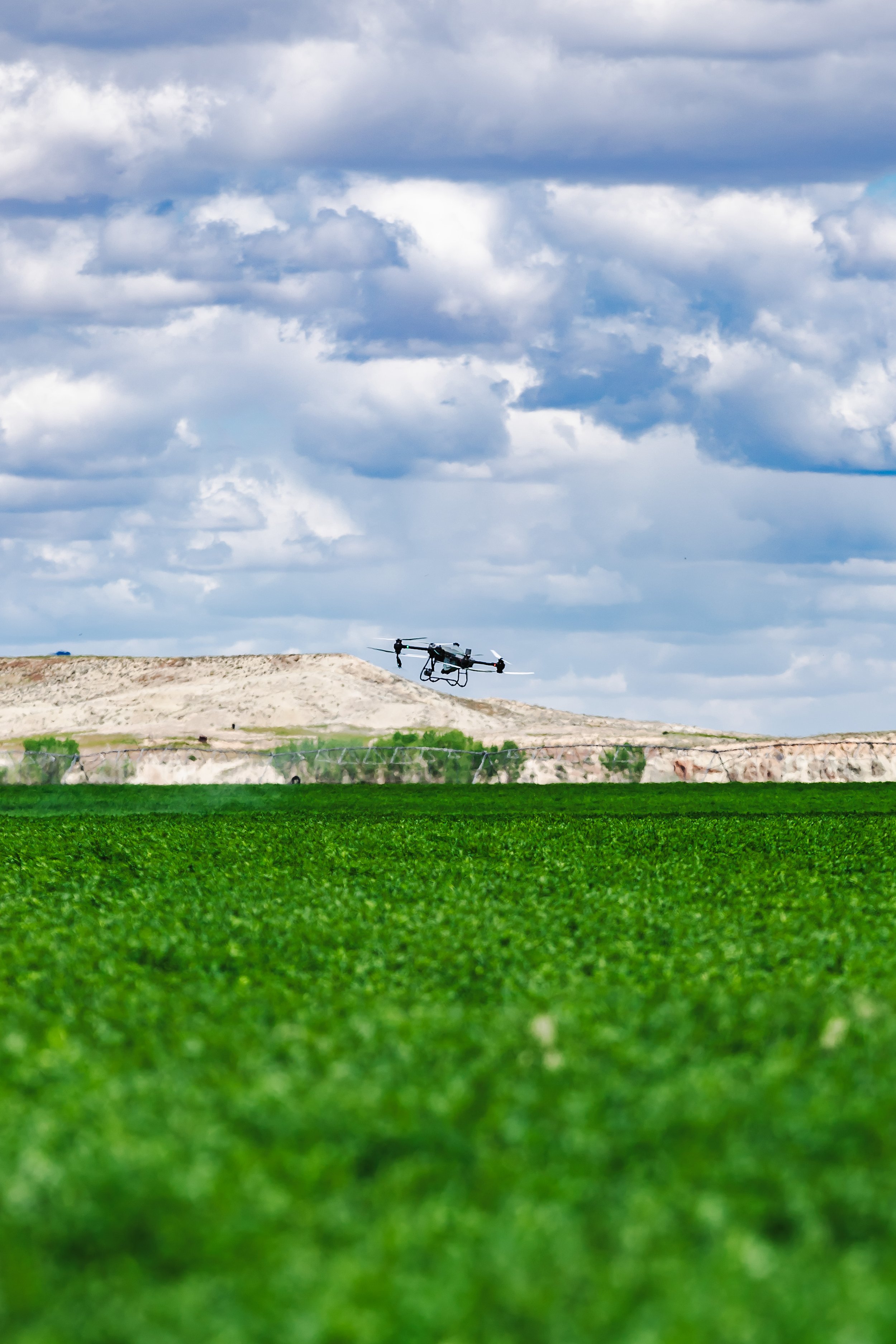 A drone flying over a green field with a cloudy sky in the background.