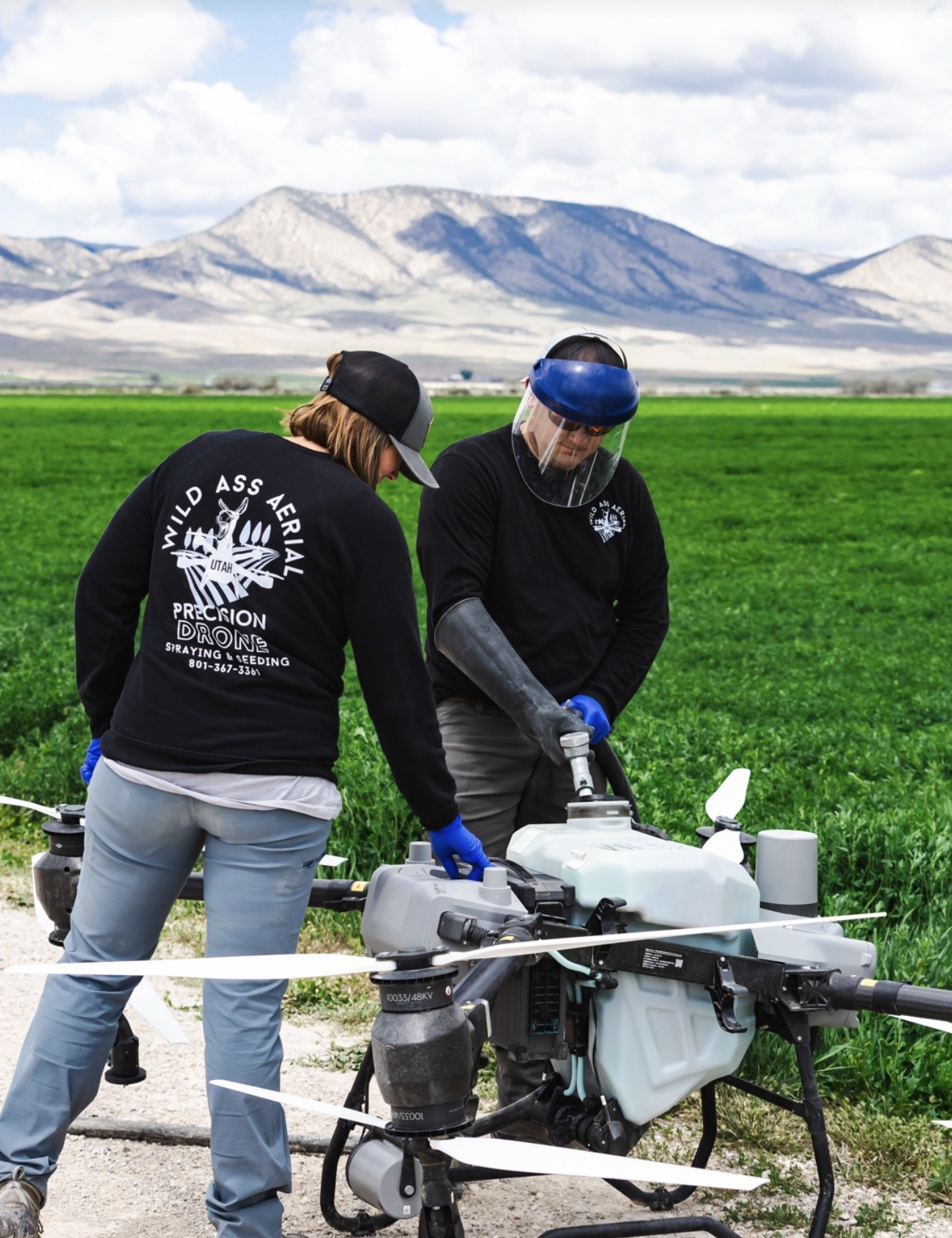 Two people working with a drone in a green field with mountains in the background.