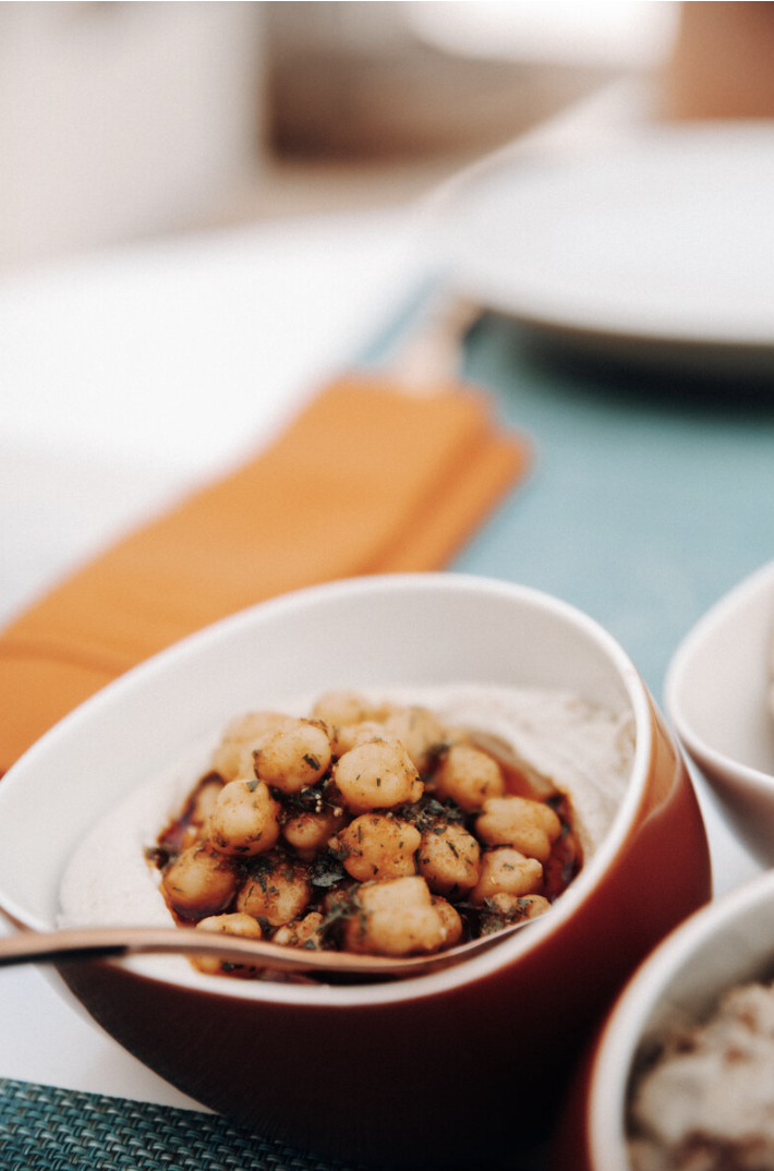 A bowl of chickpeas with herbs in sauce on a table.