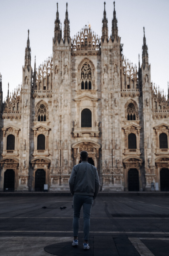 A person standing in front of the Milan Cathedral, a large Gothic-style church with intricate architecture and spires.