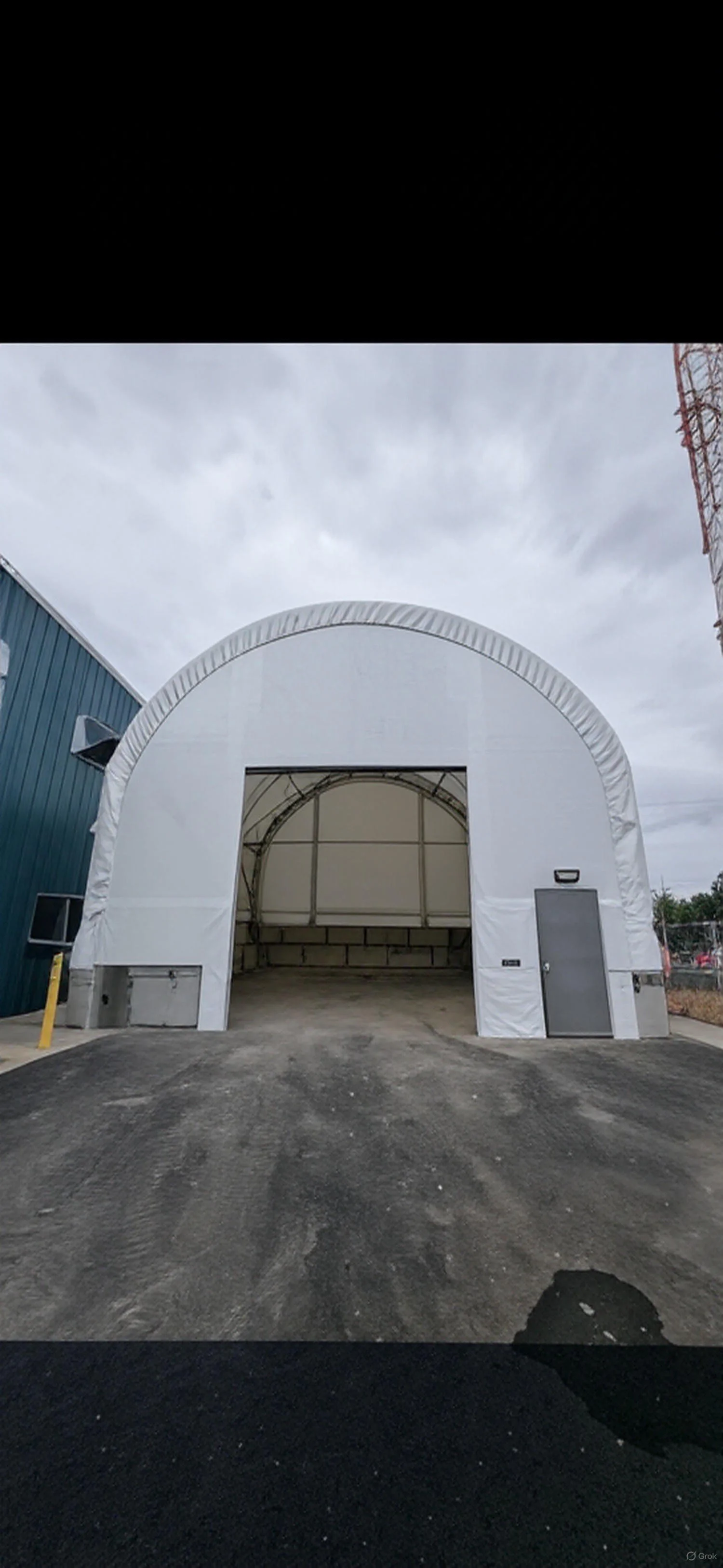 A white, inflatable structure resembling a tent or small warehouse with a large open doorway, situated outdoors on a paved surface under an overcast sky.
