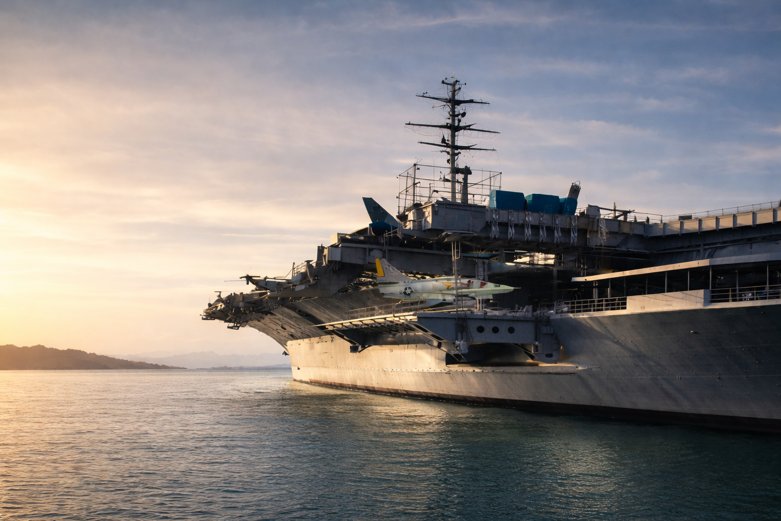 Close-up of a large aircraft carrier at dock, with military jets on the deck, during daylight.