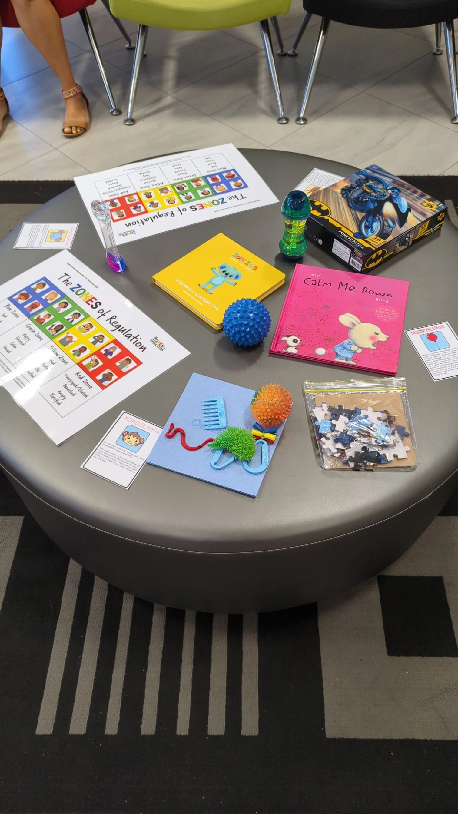 Table with children's educational toys and activity materials, including books, puzzles, sensory balls, and educational posters about zones of regulation.