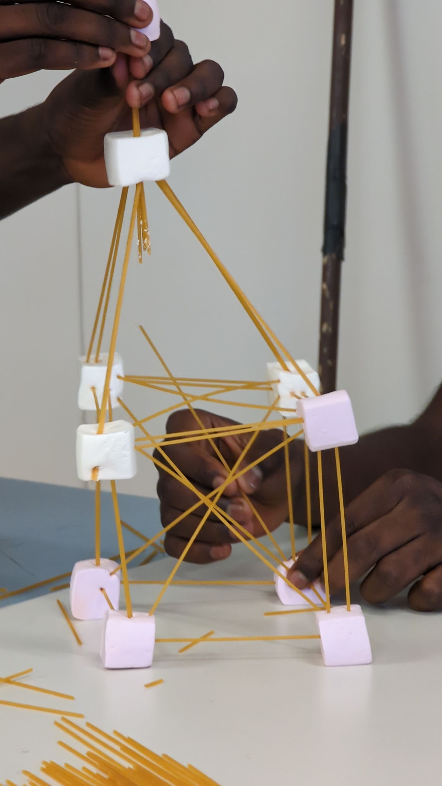 Person building a structure using spaghetti, marshmallows, and foam blocks.