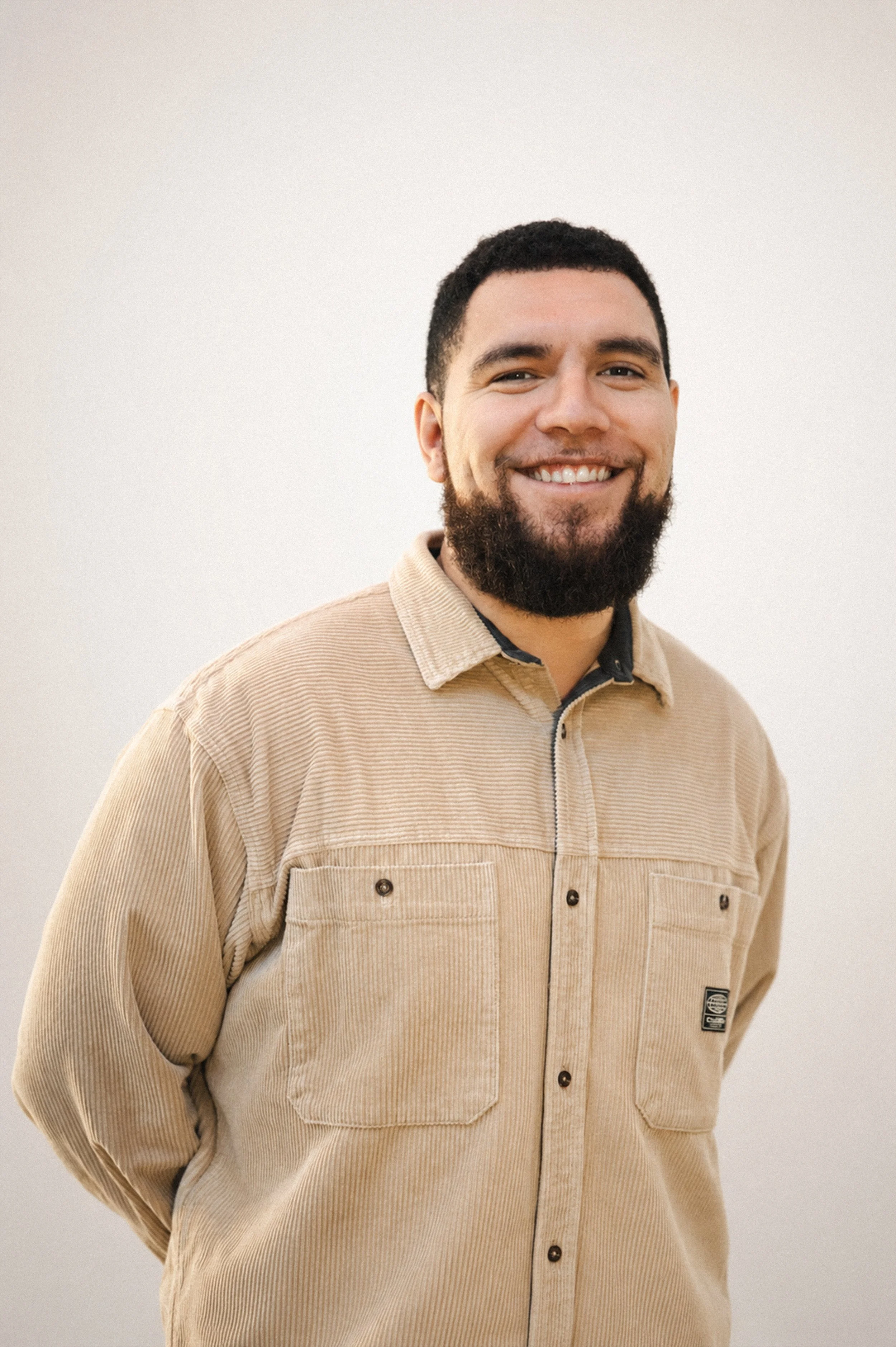 Jacob McGregor (director of AWE) is standing in front of a white background smiling at the camera with his behind his back