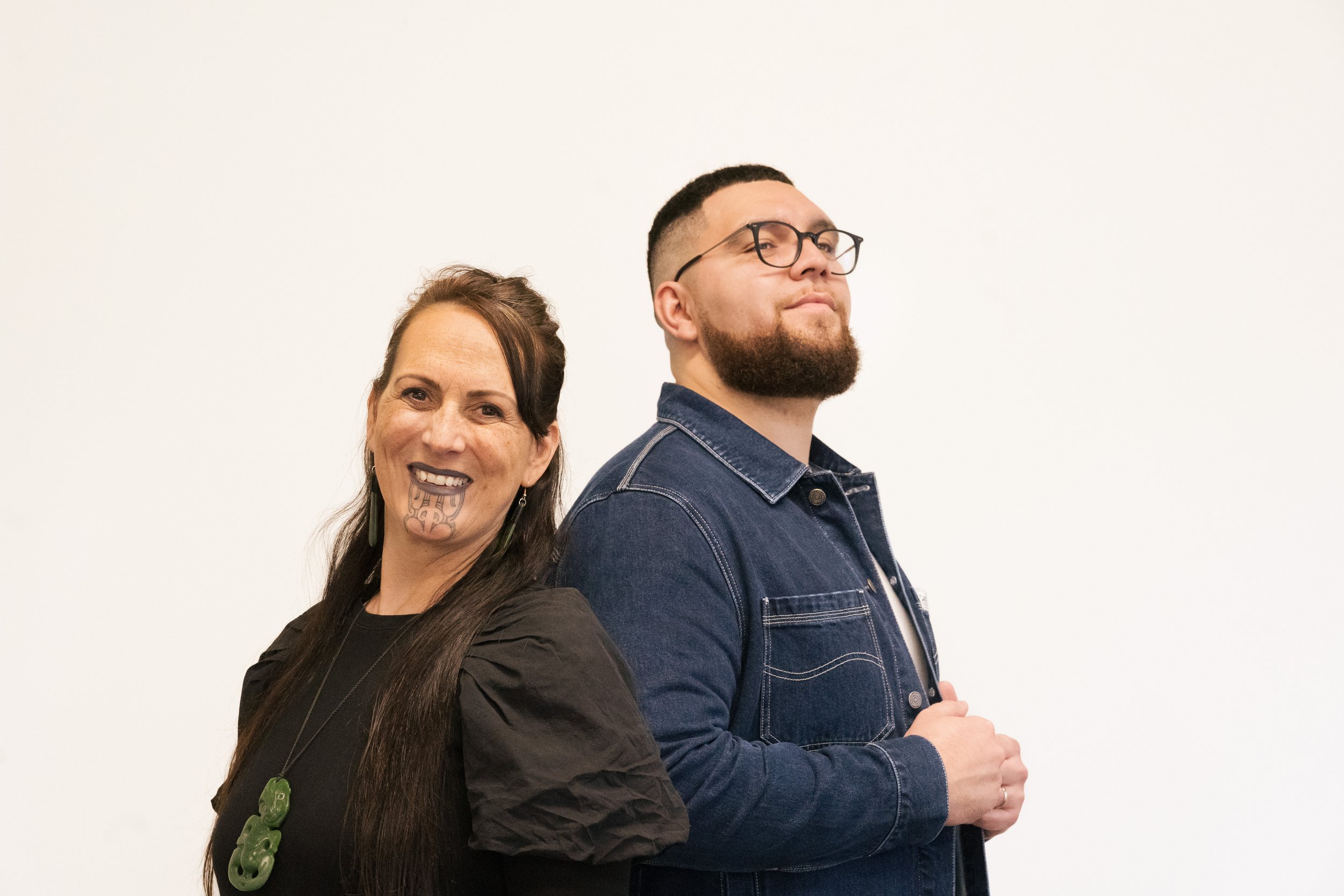 Jacob McGregor (Director) and Nicky Birch (Pou Kōrero) standing proud in front of a blank background. Jacob is looking off to the side and Nicky is looking straight at the camera.