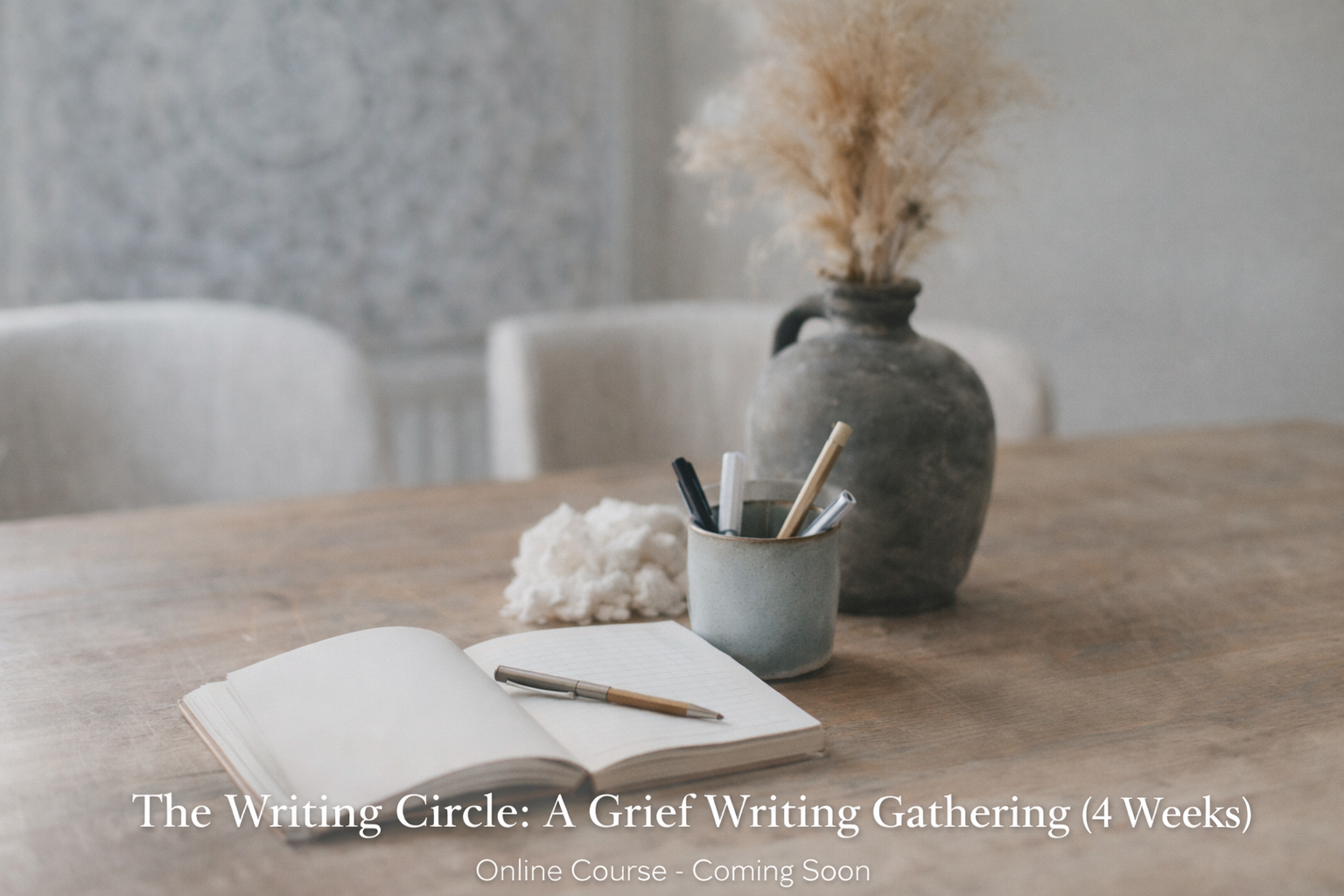 A wooden table with an open book, pens in a clear container, a notecard titled 'BE STILL', a mug with a spoon, and a large vase with dried pampas grass in a cozy, minimalist setting.