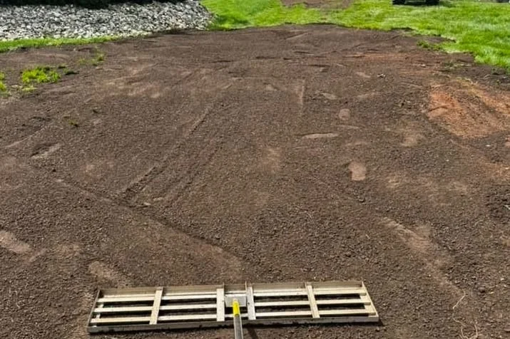 Freshly leveled soil on a backyard lawn with a leveling tool in the foreground.