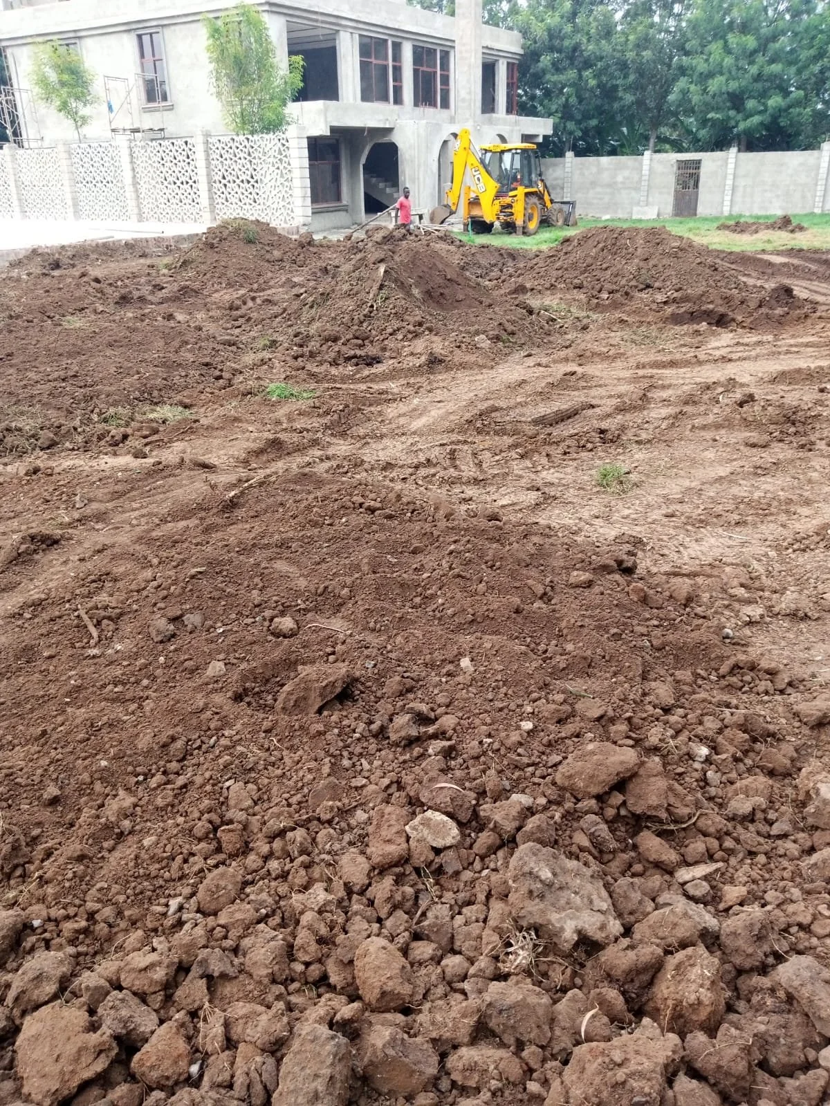 Construction site with dug-up dirt, a yellow backhoe, and a partially built house in the background.