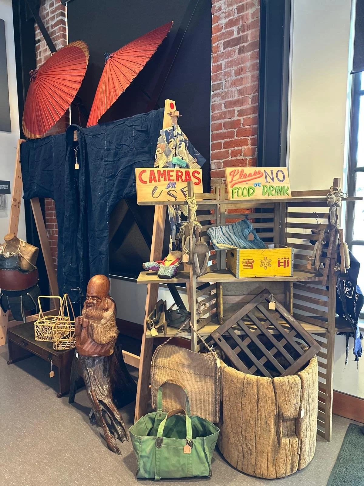 Display of a Japanese indigo-dyed garment presented with folk objects and utilitarian baskets, emphasizing traditional materials, hand stitching, and wear from use.