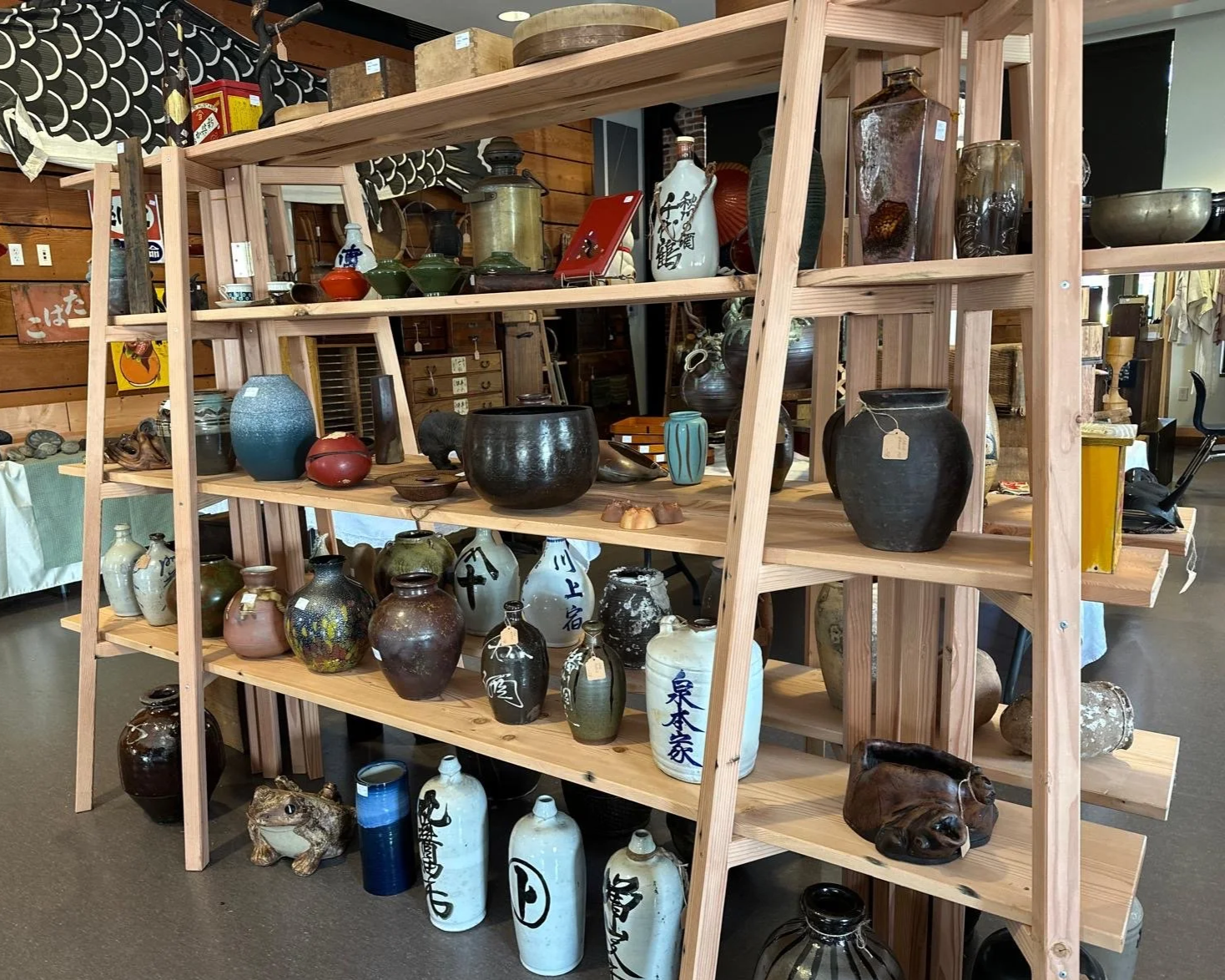Open shelving display of Japanese antique ceramic vessels, including storage jars, bottles, and utilitarian forms, highlighting varied glazes, patina, and everyday craftsmanship.