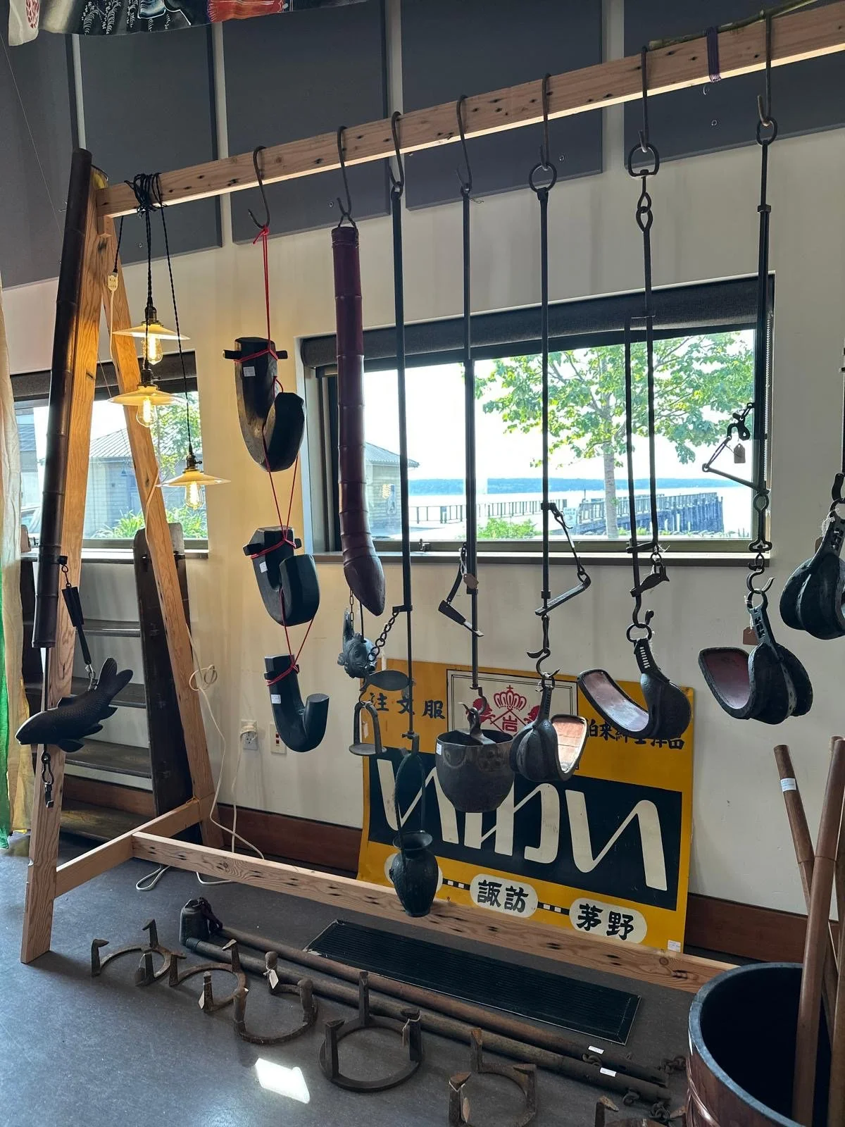 Installation of Japanese antique jizaikagi and forged iron hearth tools suspended from a wooden beam, traditionally used in irori hearths for cooking and heating.