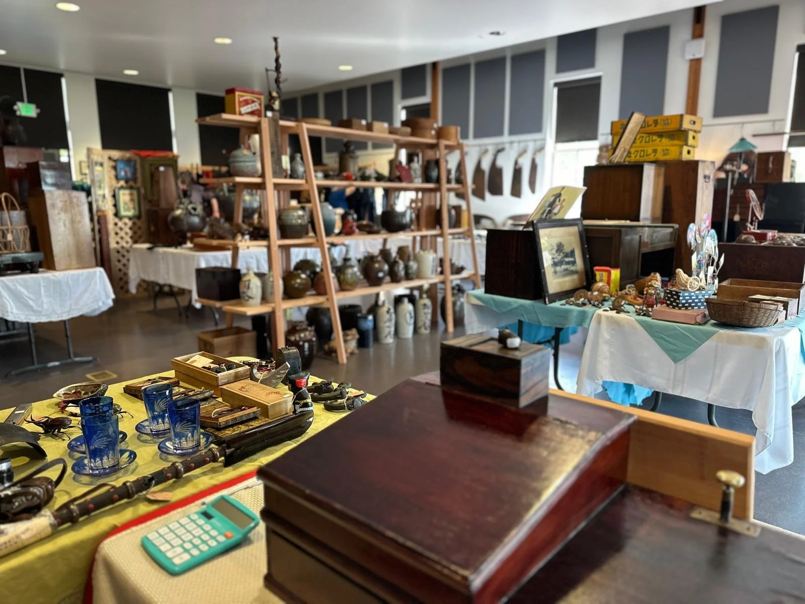 Wide interior view of a Japanese antiques pop-up featuring open shelving, ceramics, tools, small objects, and furniture arranged across multiple display tables.