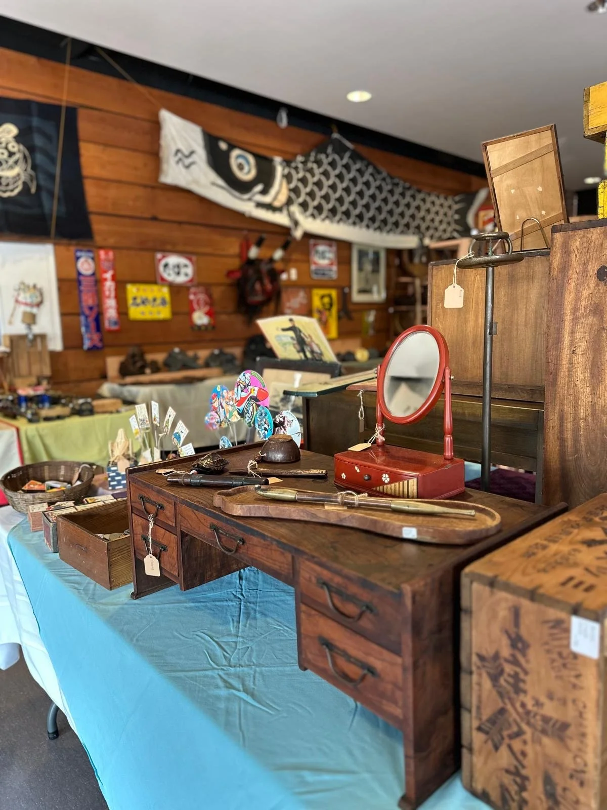 Display of a Japanese antique writing desk with drawers, accompanied by personal objects including a vanity mirror, tools, and small containers, arranged as a functional still life.