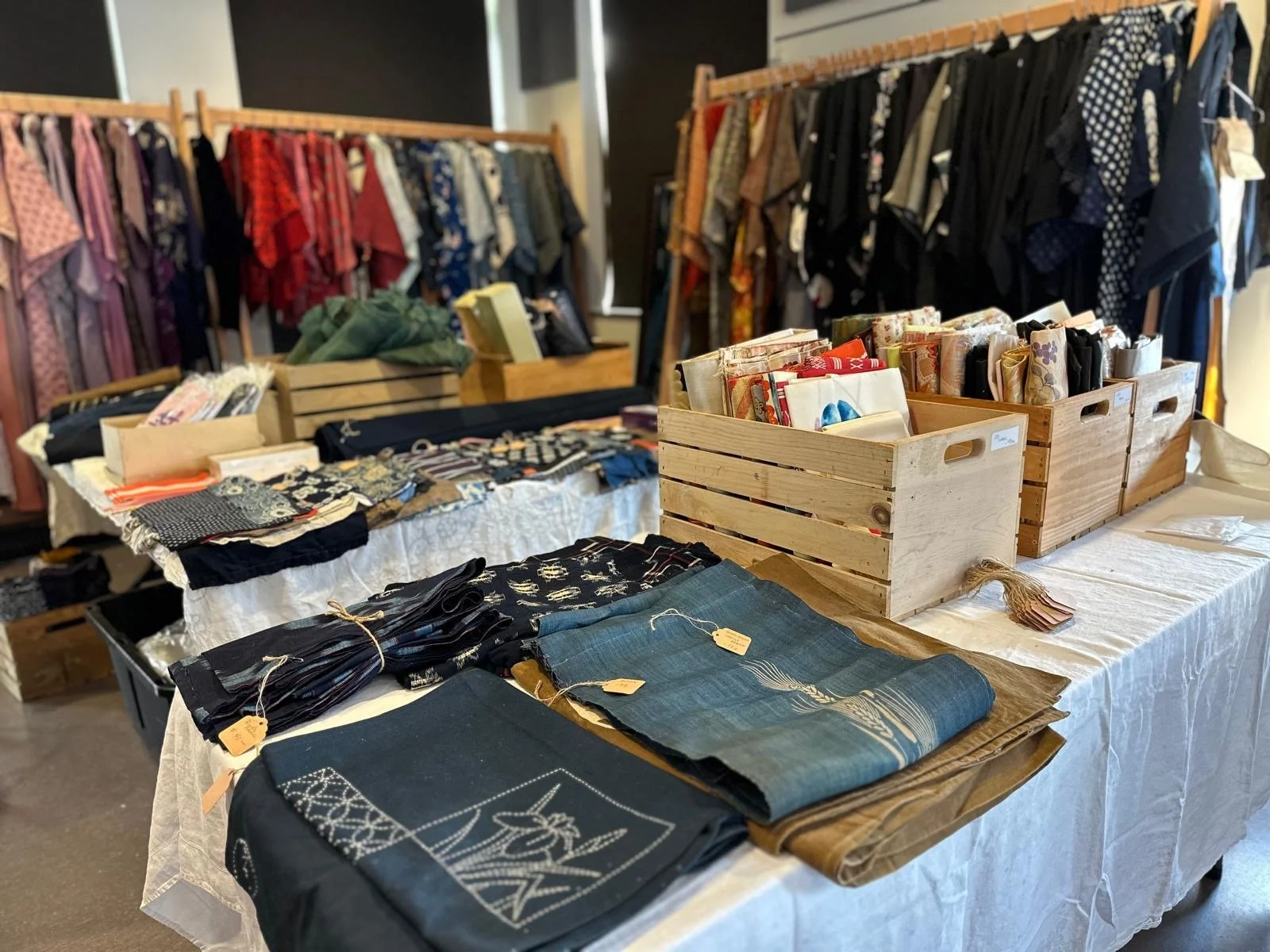 Tabletop display of Japanese antique textiles and folded fabrics arranged by color and pattern, reflecting everyday clothing and household use.